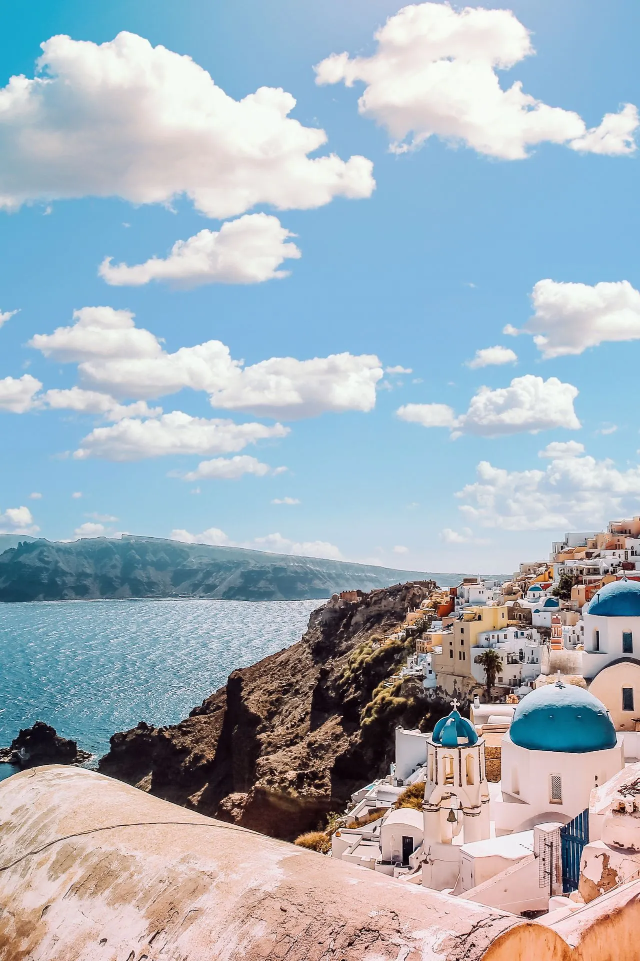 "Iconische witte huizen met blauwe koepeldaken op een klif aan de Egeïsche Zee, typisch voor Santorini in Griekenland. Adembenemend uitzicht op helderblauw water en een pittoresk dorp onder een zonnige hemel met wolken. Perfect voor een romantische vakantie, culturele ontdekking en fotografie. Ontdek Griekse architectuur, mediterrane charme en spectaculaire zonsondergangen. Ideaal voor reizigers die houden van zon, zee en authentieke cultuur."