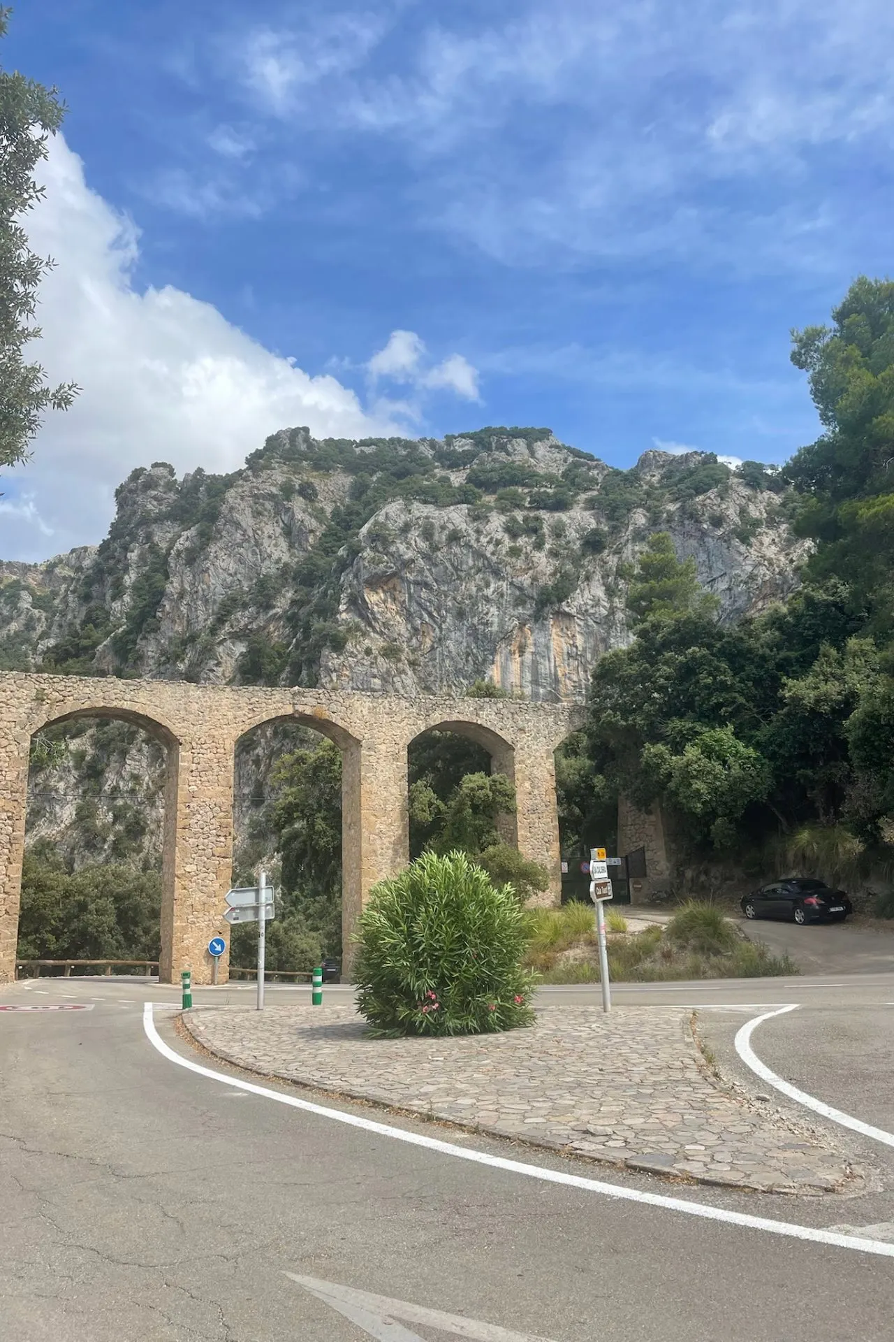 Een eeuwenoude stenen aquaductbrug met drie grote bogen, gelegen aan de voet van steile rotsen in het berglandschap van Serra de Tramuntana.