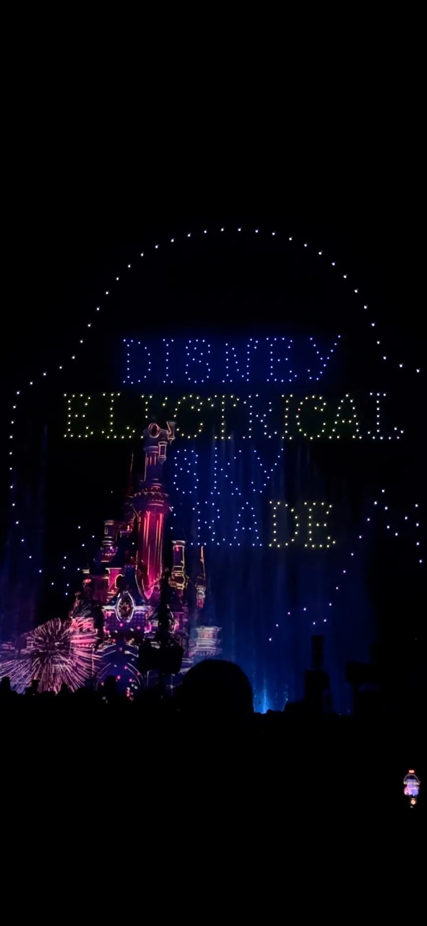 Disney Electrical Sky Parade lichtshow bij het Doornroosje kasteel in Disneyland Parijs, met kleurrijke projecties en fonkelende lichtletters tegen een donkere nachtelijke hemel.