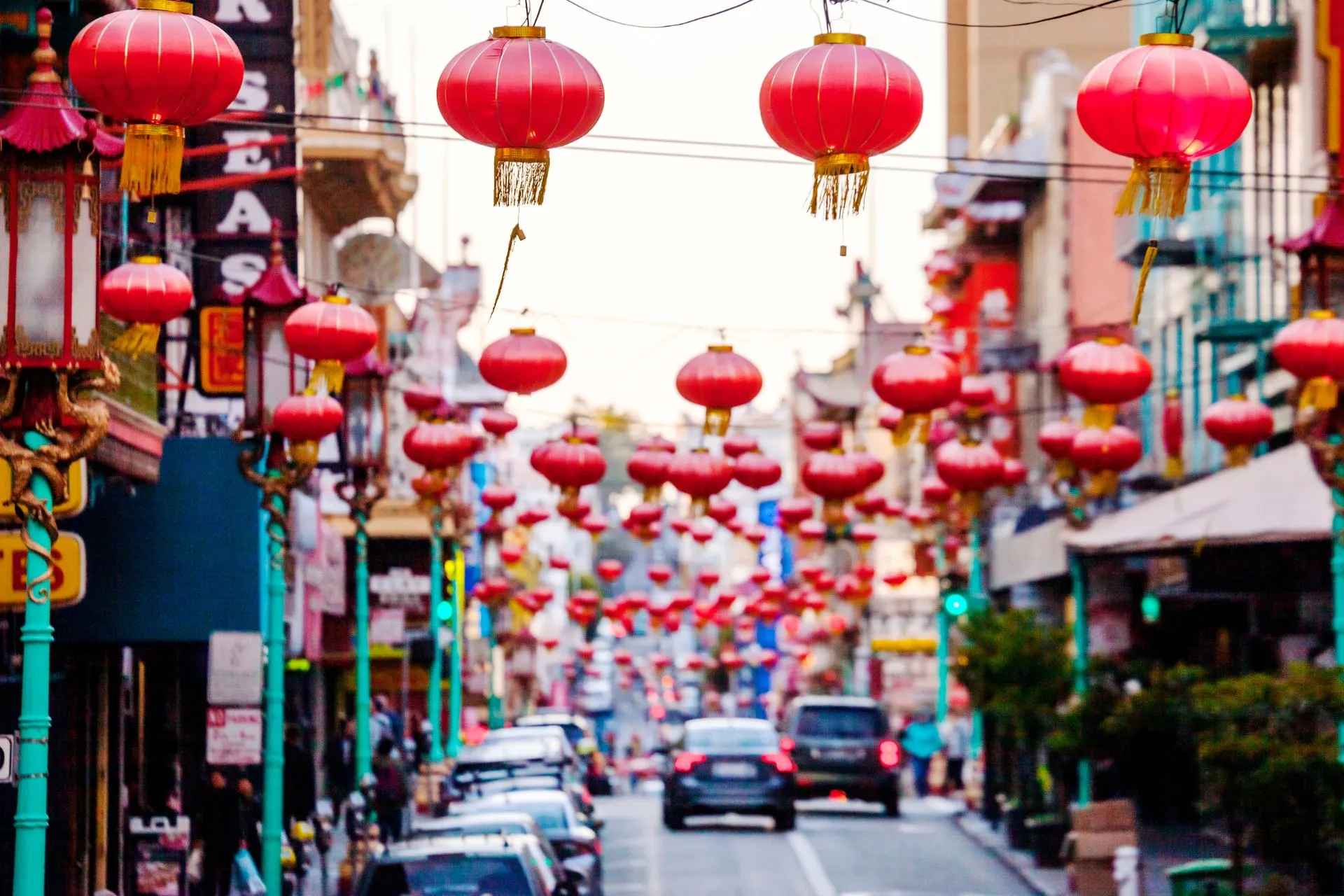 Straat in Chinatown met rode Chinese lantaarns, winkels met Chinese tekens en geparkeerde auto's – levendige sfeer in San Francisco.