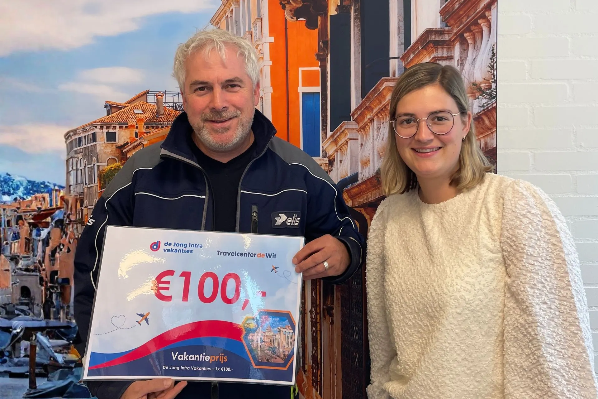 Man en vrouw tonen een De Jong Intra Vakanties-voucher van €100 tijdens de prijsuitreiking van de winactie bij Travelcenter de Wit Gemert.