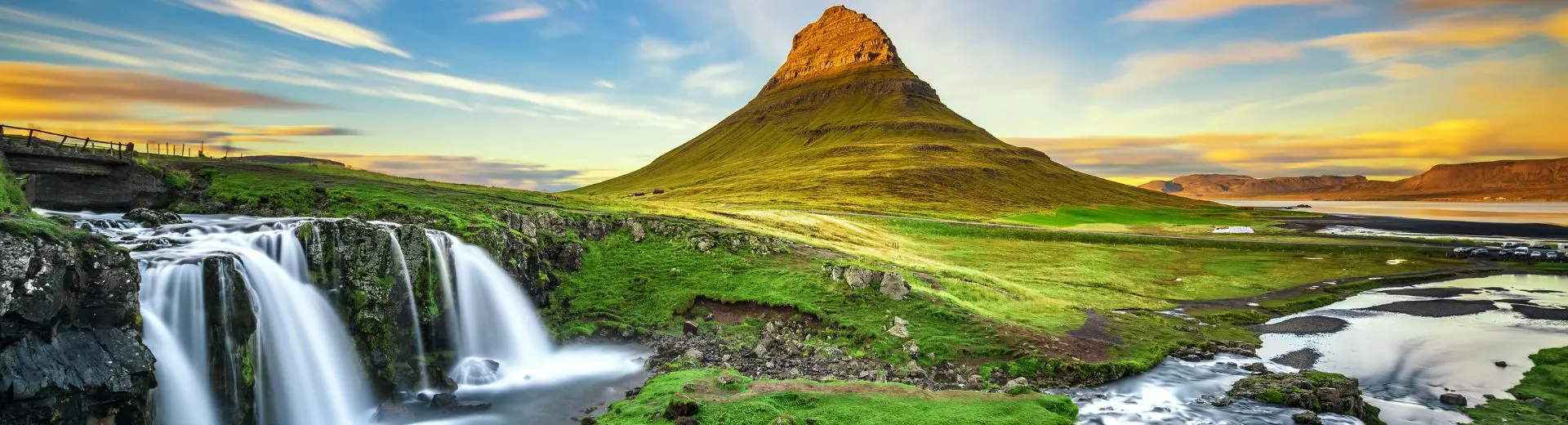 Het iconische Kirkjufell-gebergte in IJsland, met een waterval op de voorgrond en een kleurrijke lucht bij zonsondergang.