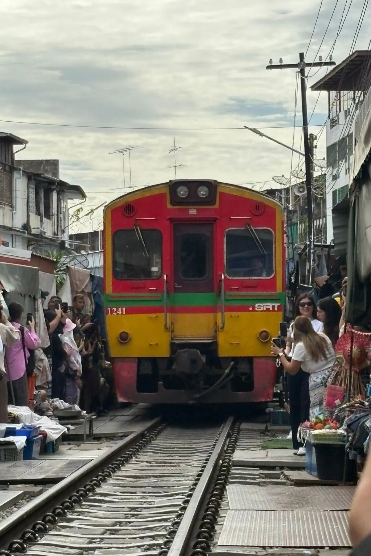 Twee mensen dragen schorten van Zabb-E-Lee Thai Cooking School en bereiden gerechten op een kookstation in een open bamboepaviljoen.