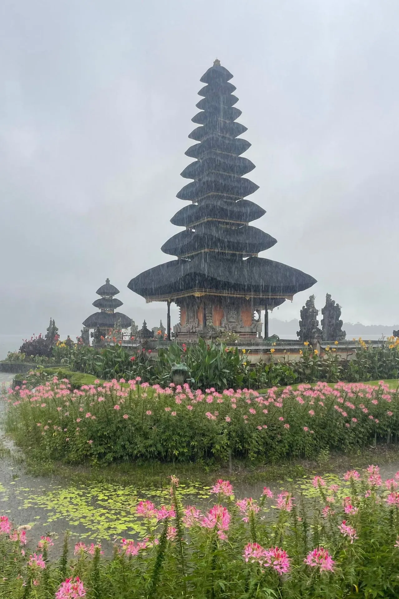 Pura Ulun Danu Bratan tempel op Bali, omringd door bloemen en vijvers tijdens een lichte regenbui.