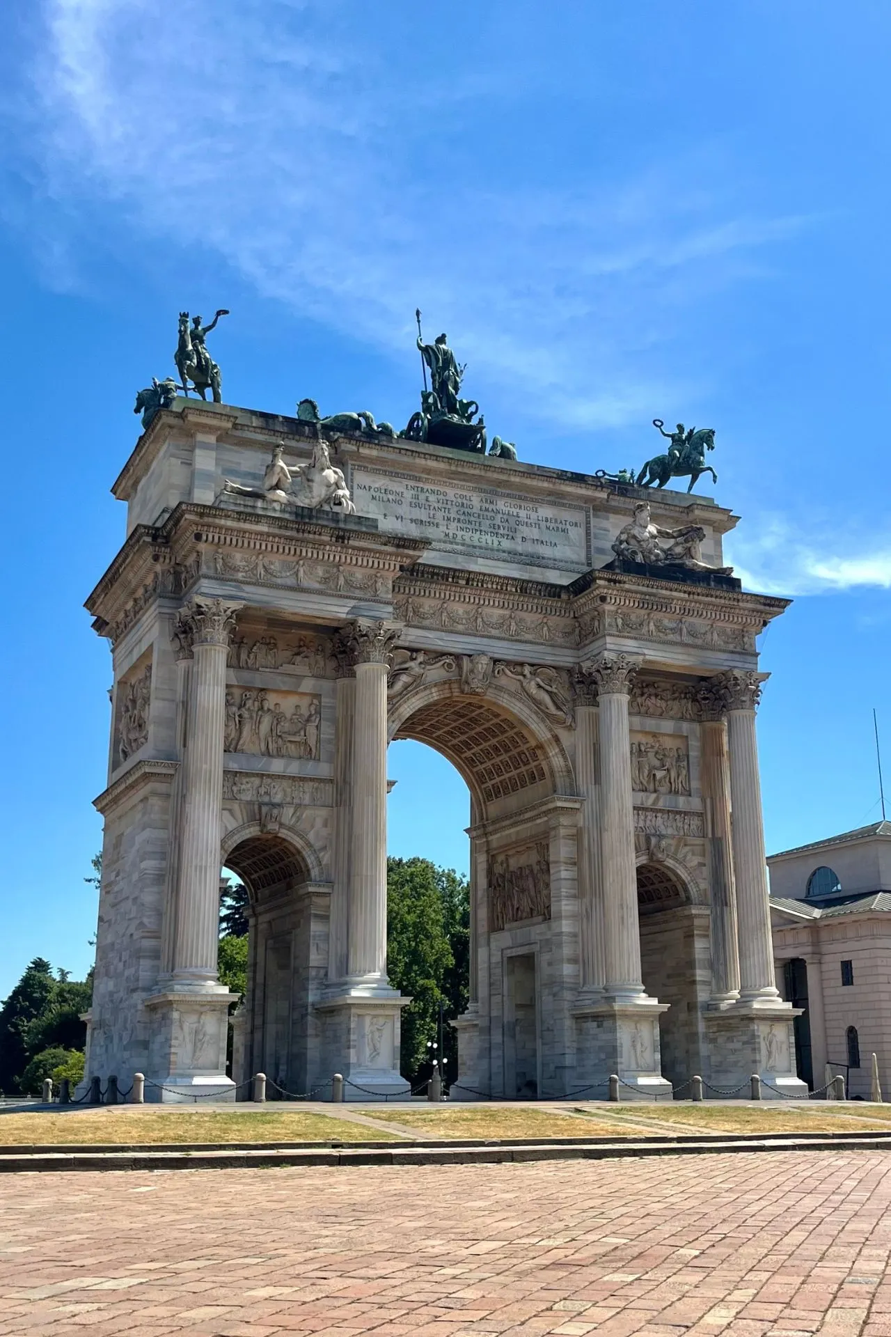 De Arco della Pace in Milaan, een triomfboog uit de 19e eeuw met indrukwekkende zuilen, reliëfs en beelden, waaronder een vierspan op de top, onder een heldere blauwe hemel.