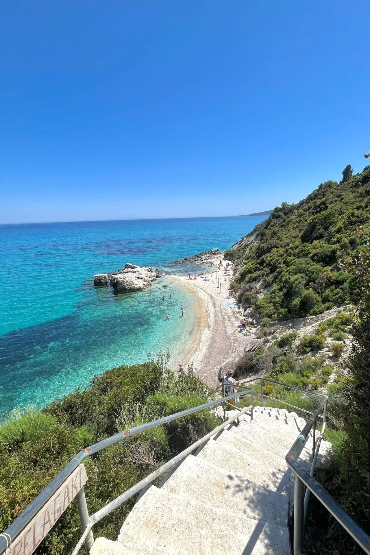 Uitzicht vanaf een trap naar een afgelegen strand met turquoise water en groene heuvels op Zakynthos.