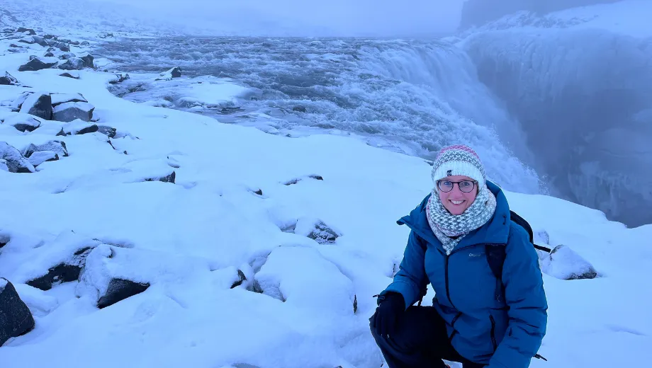 Reiziger geknield in de sneeuw bij de winterse Dettifoss‑waterval in Noord‑IJsland.

