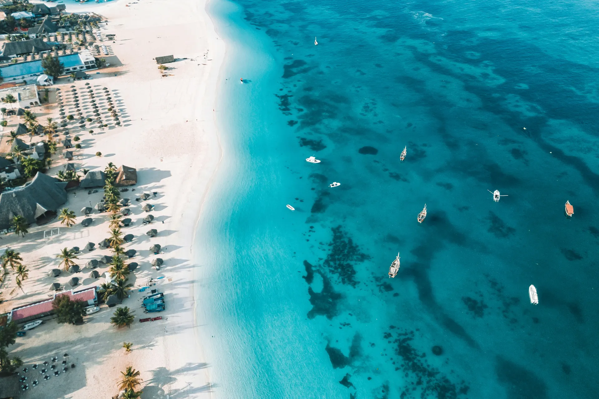 Helderblauwe oceaan en wit strand bij Nungwi op Zanzibar, gezien van boven met vissersbootjes.