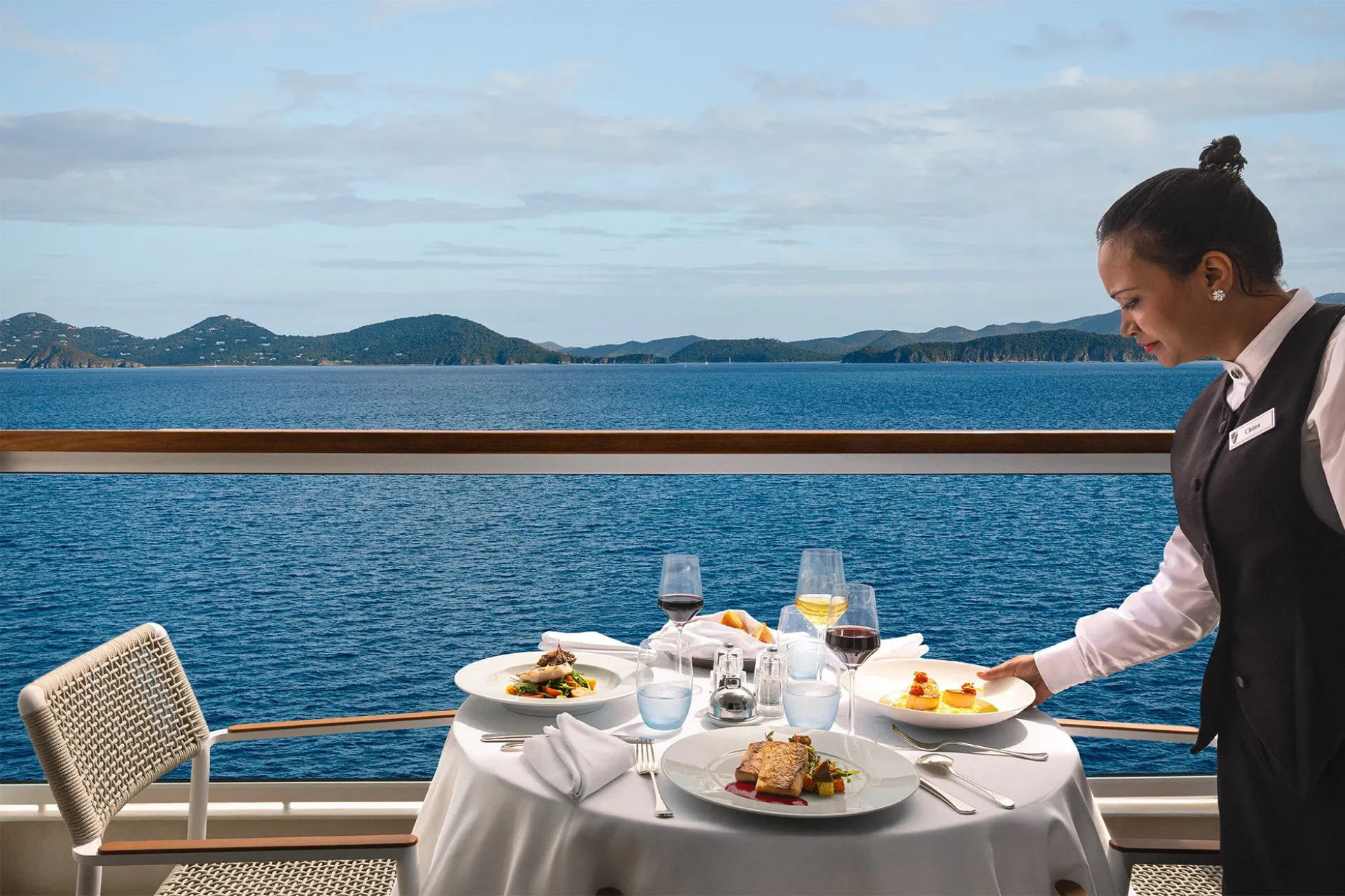 Persoonlijke bediening bij een privé diner op het balkon van een Veranda Suite aan boord van een Holland America Line cruiseschip met uitzicht op zee.