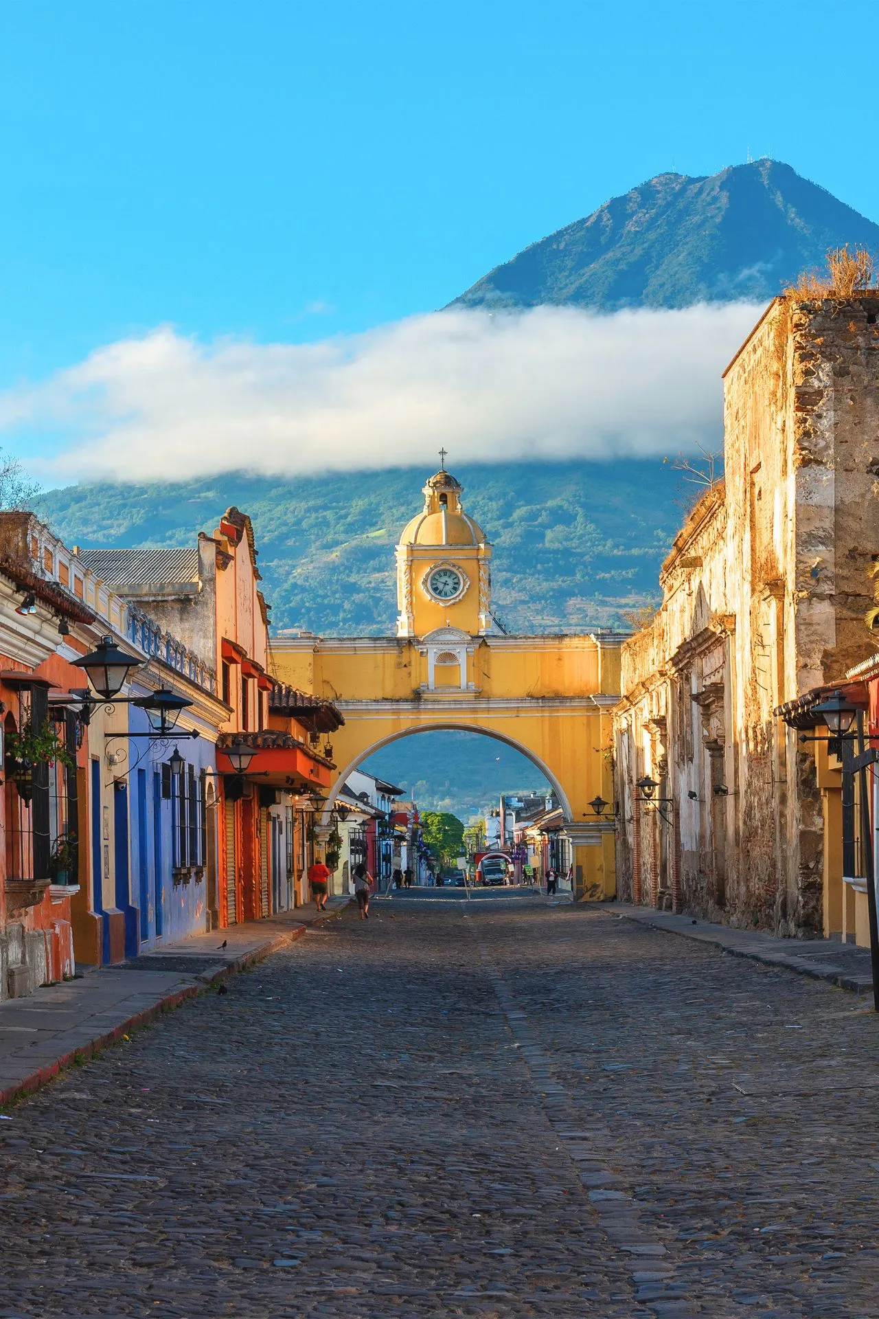 De Santa Catalina‑boog in Antigua, met kleurrijke koloniale huizen en de Volcán de Agua op de achtergrond.
