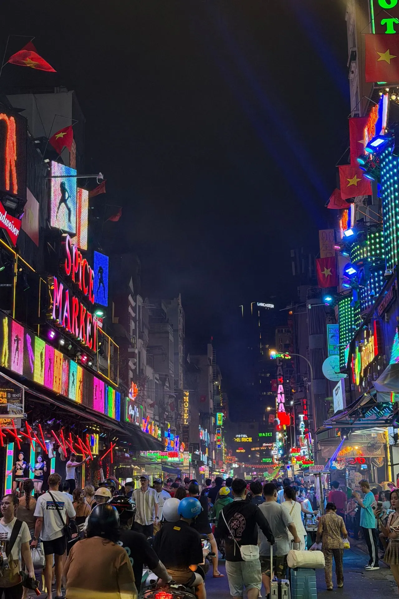 Drukke straat in het centrum van Ho Chi Minhstad bij avond, met kleurrijke neonverlichting, restaurants, barretjes en een mix van voetgangers en scooters. Deze levendige wijk staat bekend om haar bruisende sfeer en laat het moderne en energieke Vietnam zien.