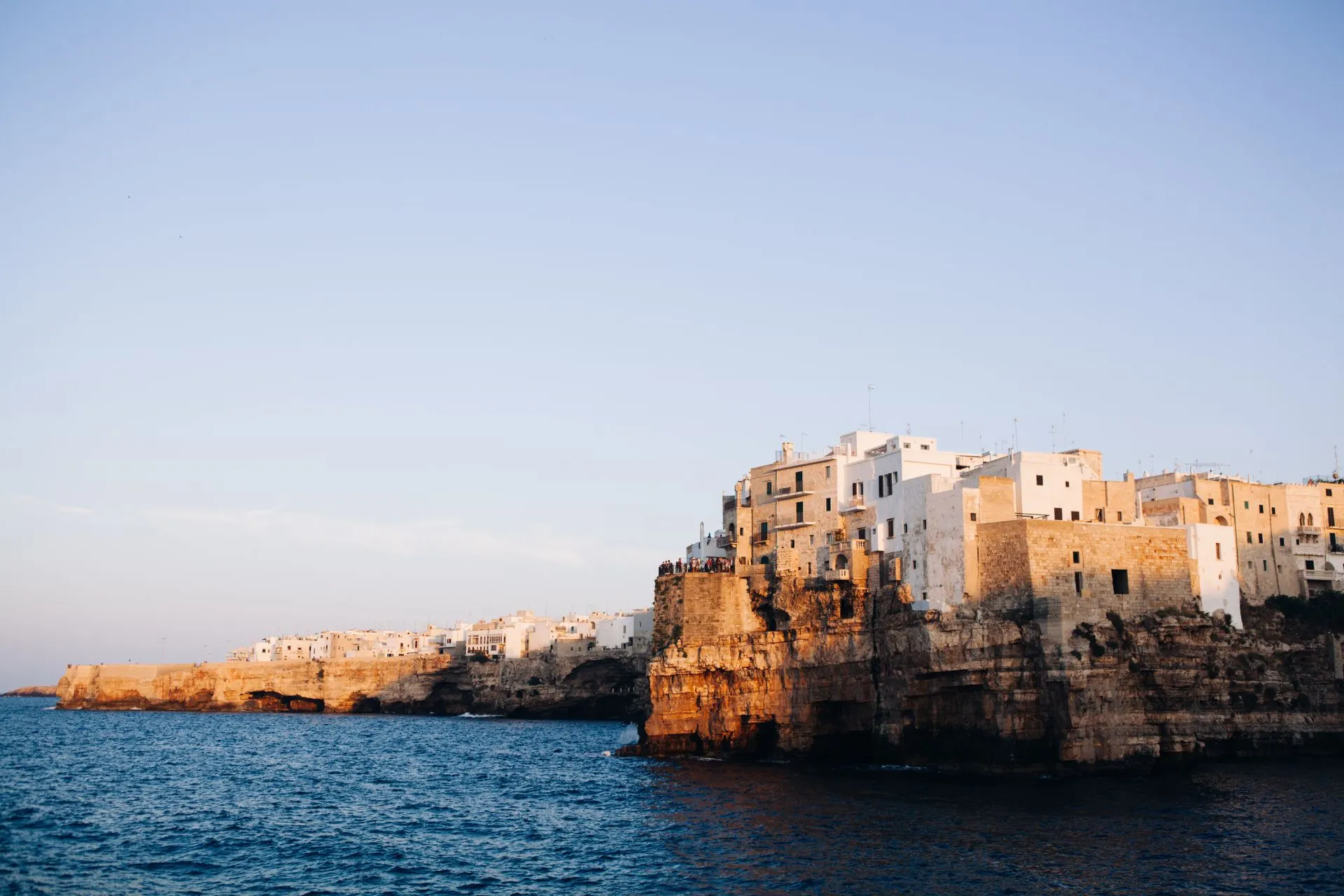Uitzicht op de historische kuststad Polignano a Mare in Puglia, Italië, met witte huizen gebouwd op steile kliffen die uitkijken over de blauwe Adriatische Zee in het warme avondlicht.