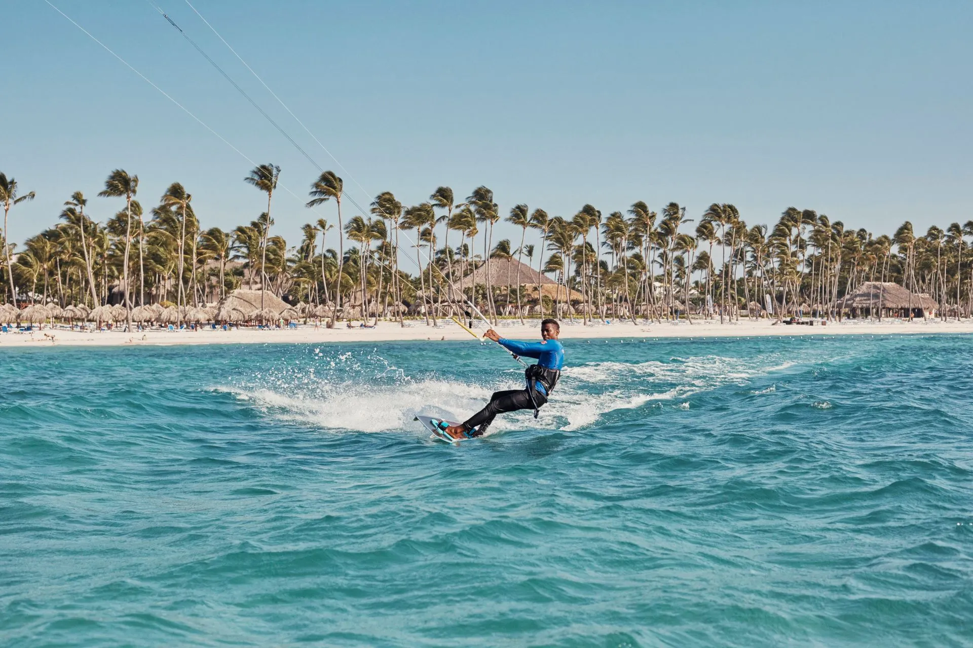 Watersport bij Club Med: kitesurfer op helderblauw water met palmbomen op de achtergrond in een tropisch all-inclusive resort. Ontdek Club Med zonvakanties in de Caraïben, Malediven of Bali met onbeperkte sportactiviteiten en luxe faciliteiten.