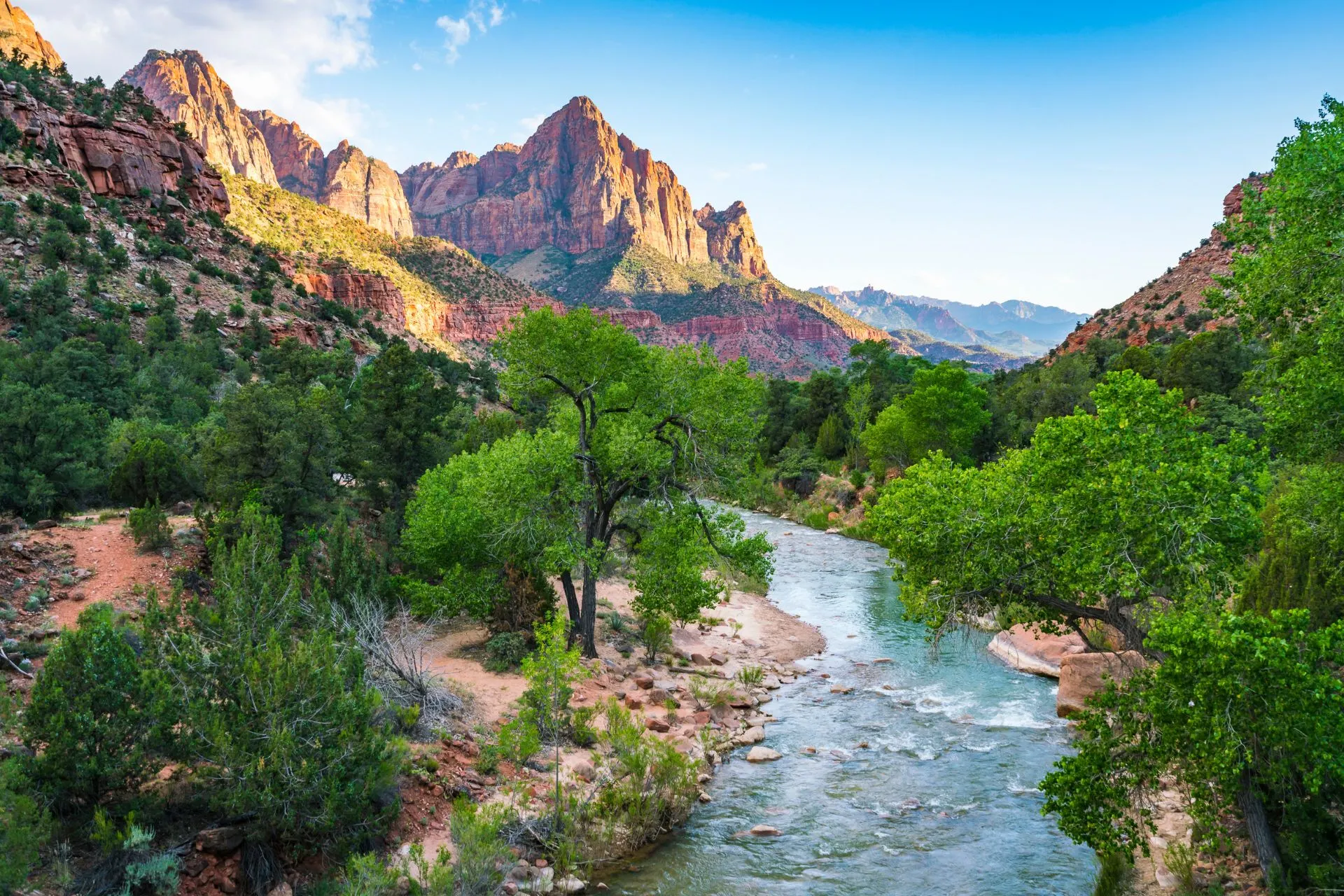 Groene rivier die door een vallei stroomt, omringd door imposante rode bergen in Zion National Park. Dit park combineert ruige natuur met serene uitzichten en is een van de topbestemmingen voor avontuurlijke reizigers die de nieuwe regels voor Amerikaanse nationale parken in 2026 willen volgen.