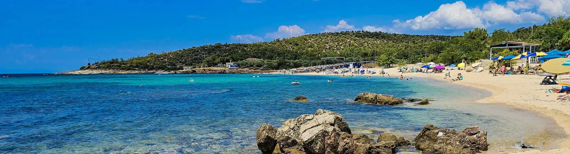 Rustig strand op het Griekse eiland Thassos met turkoois water, zandstrand en groene heuvels.
