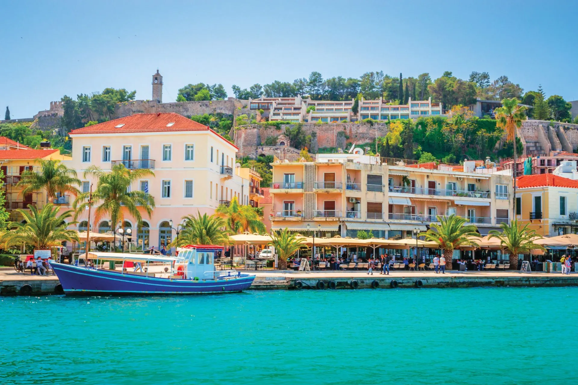 Havenpromenade van Nafplio, Griekenland met kleurrijke gebouwen, een vissersboot en een fort op de achtergrond – geliefde aanlegplaats tijdens een cruise door de Griekse eilanden.