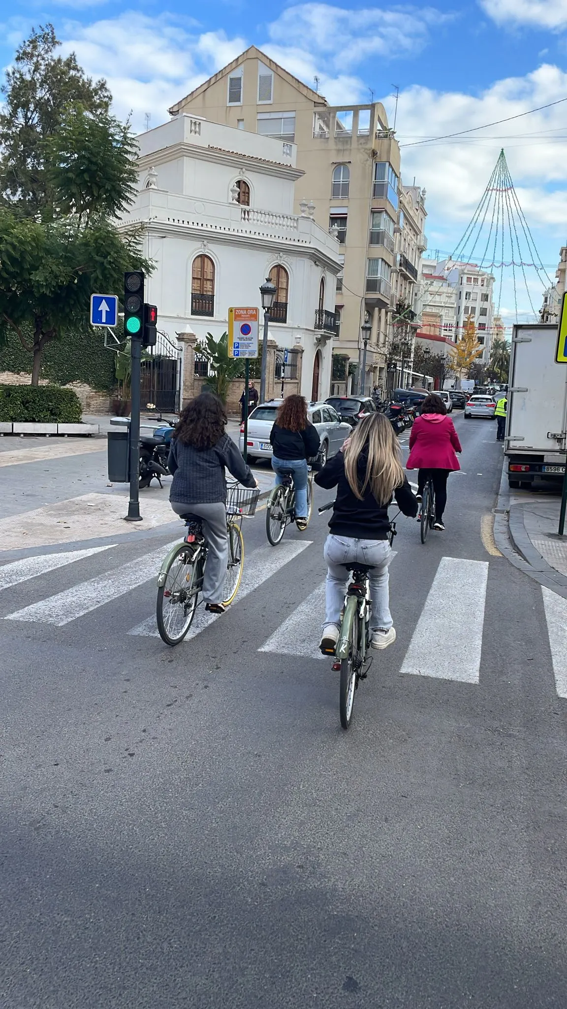 Een leuke vakantie foto waarbij een aantal dames over een weg fietsen, je iet een zebrapad en gebouwen.