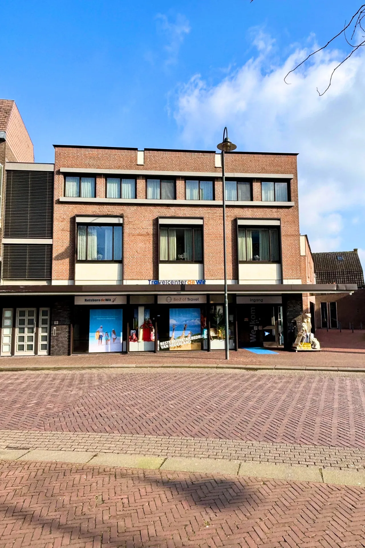 Filiaal van Travelcenter de Wit in Veghel, gefotografeerd vanaf de voorkant op een zonnige dag, met helder blauwe lucht en de gevel goed zichtbaar.
