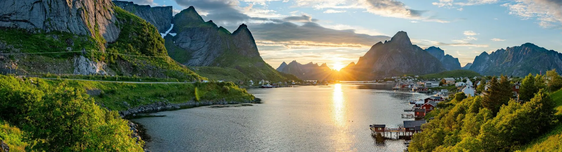 Adembenemend landschap van de Noorse fjorden met steile bergwanden, rustig fjordwater en een sfeervol dorp bij zonsondergang, een populaire bestemming voor cruises door Noorwegen langs natuur, fjorden en indrukwekkende kustlijnen.
