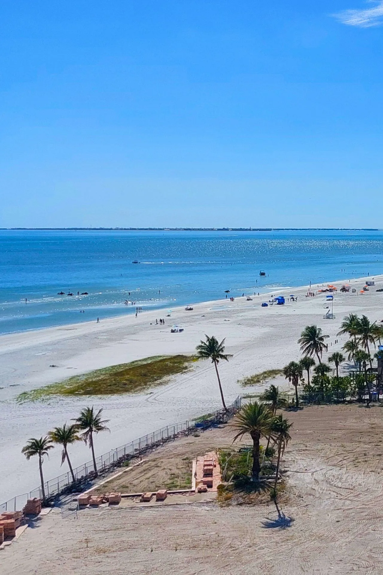 Uitzicht op een breed strand in Naples, Florida, met helderblauw water en enkele palmbomen langs de kustlijn onder een stralende lucht.