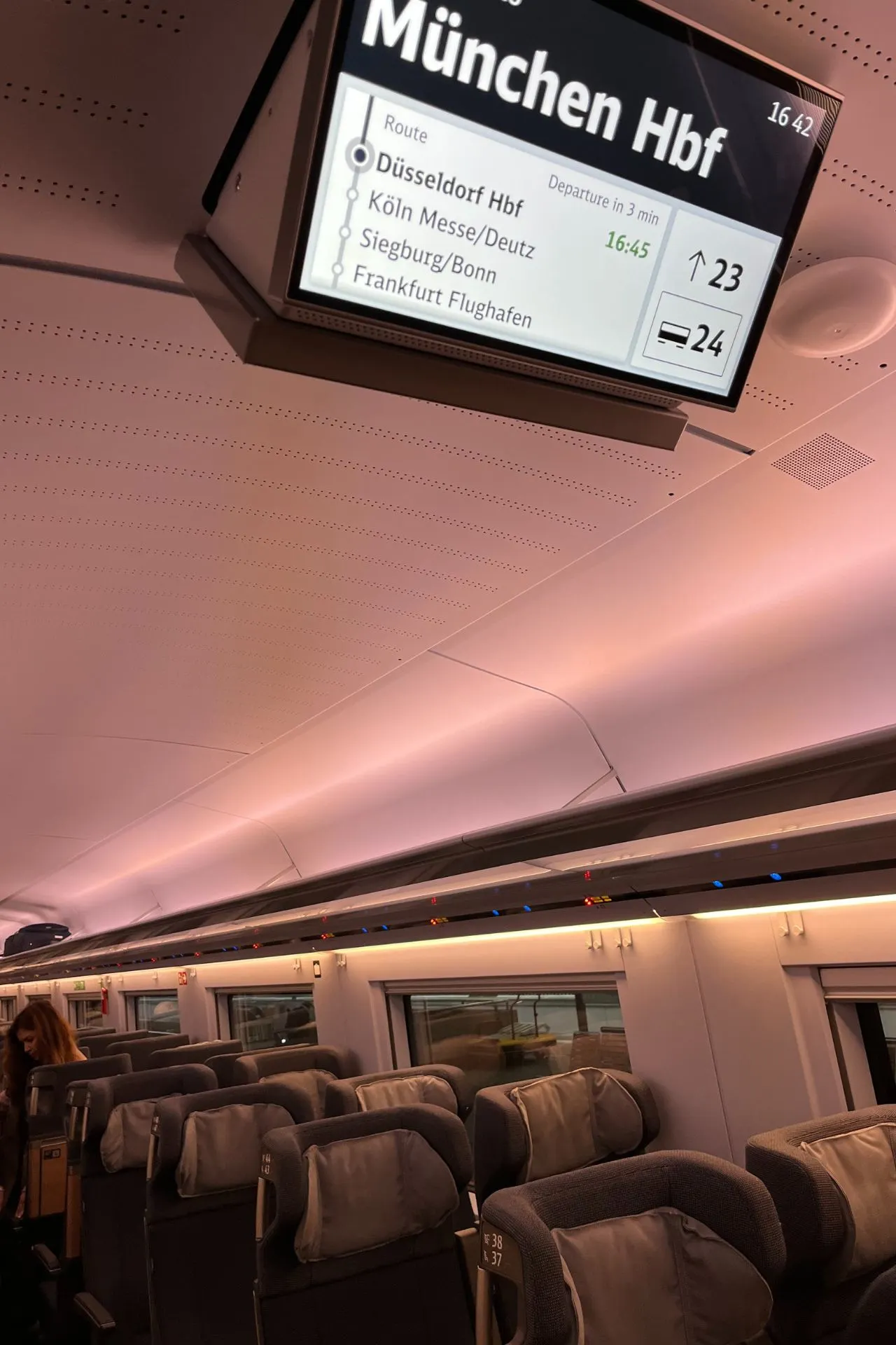 Het interieur van een ICE-trein, met comfortabele stoelen en een scherm waarop de route naar München Hauptbahnhof wordt weergegeven.