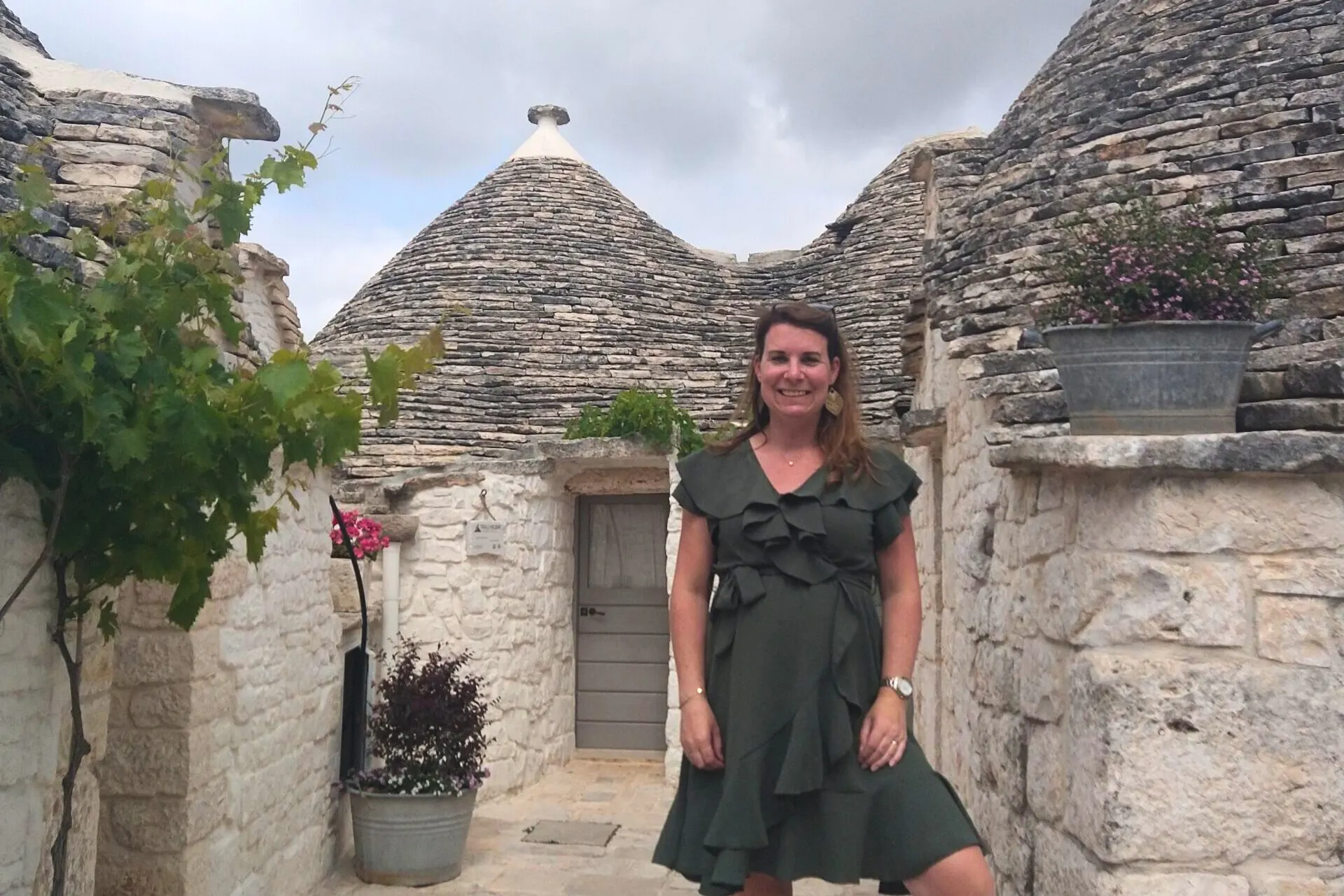 Lachende vrouw in een groene jurk poseert voor een traditionele witte trullo in Alberobello, Puglia.
