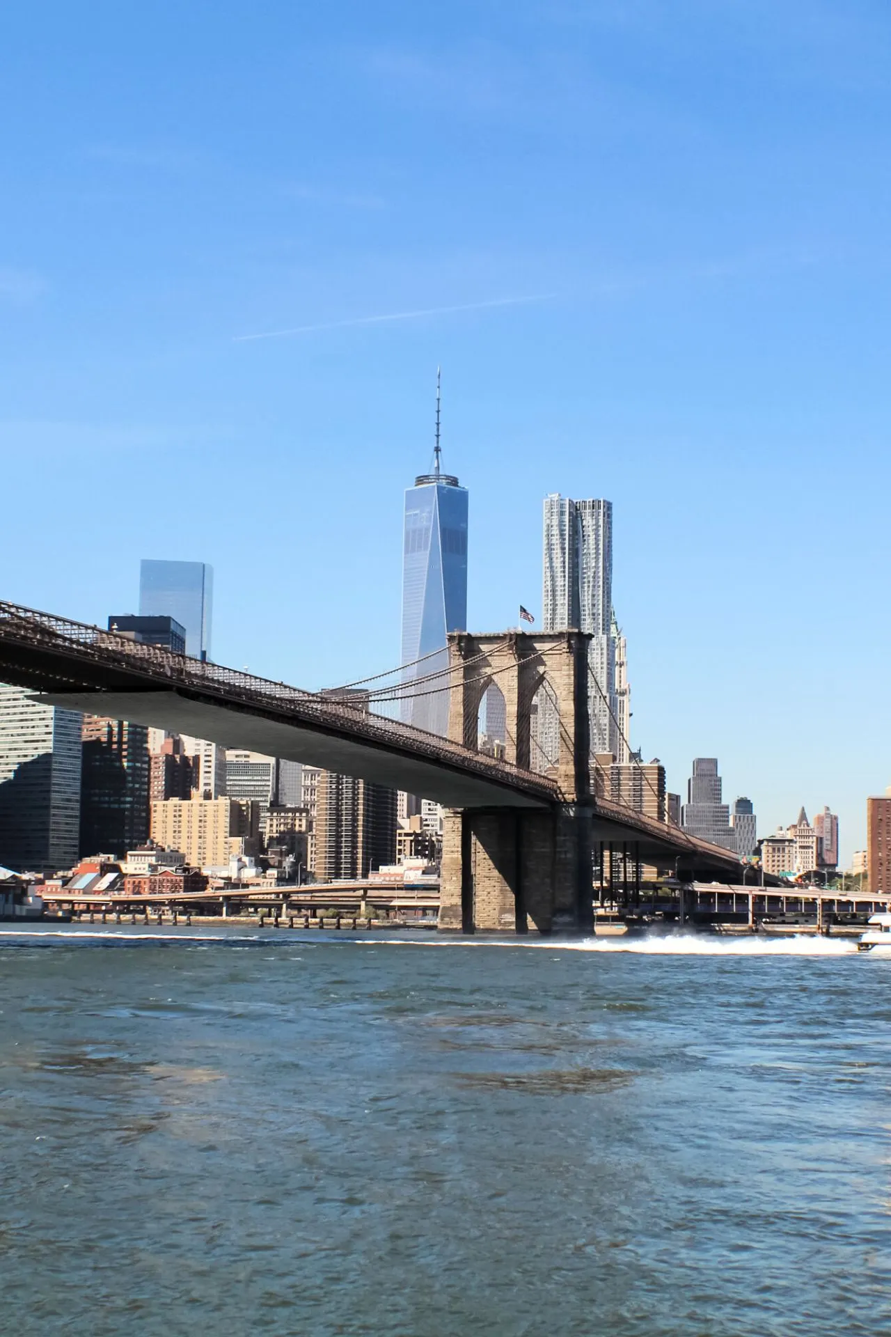 De Brooklyn Bridge in New York, gezien vanaf het water, met zijn iconische torens en kabels die de skyline van de stad doorkruisen.