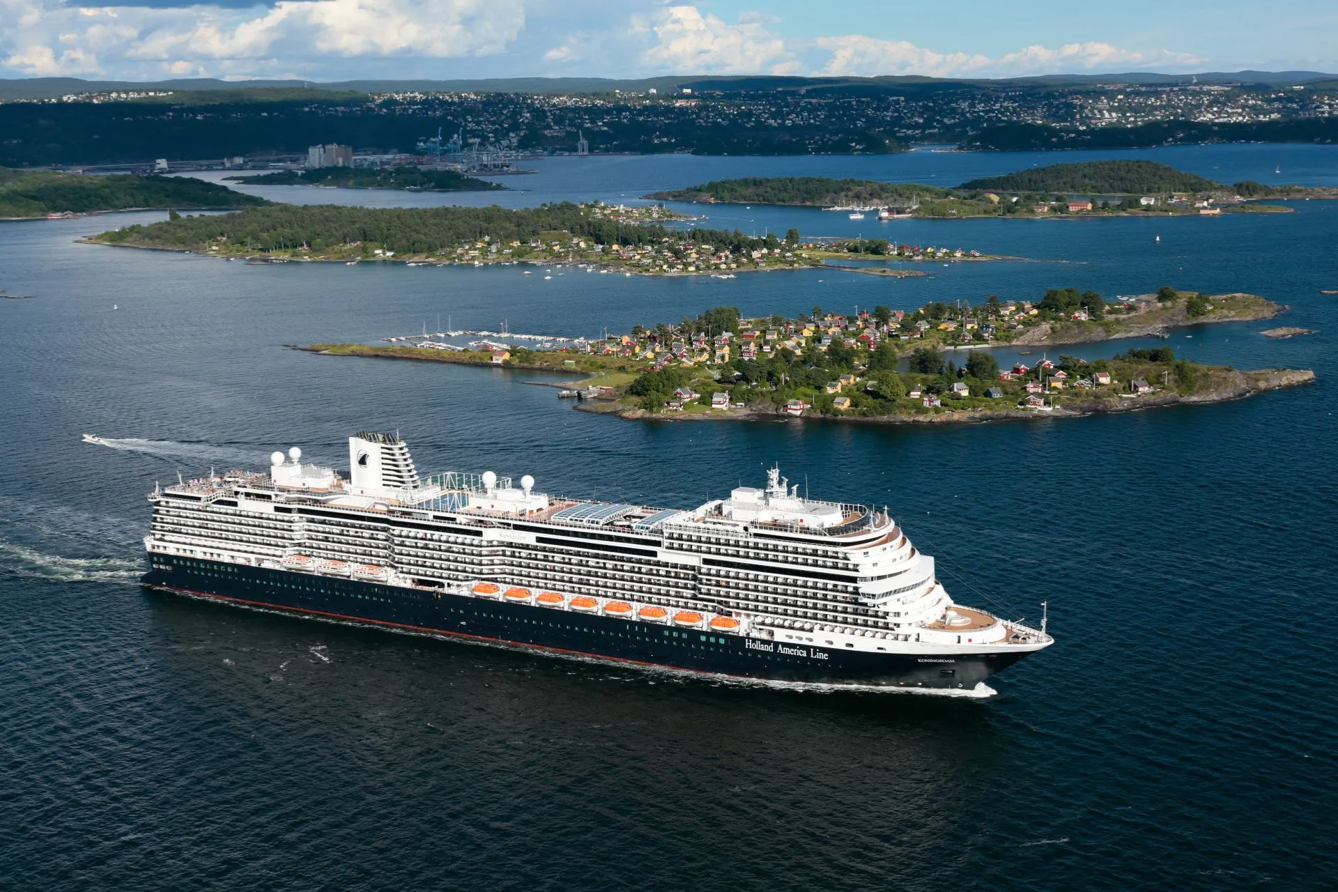 Holland America Line cruiseschip nadert Oslo met uitzicht op eilandjes met gekleurde huisjes en de stad in de verte.