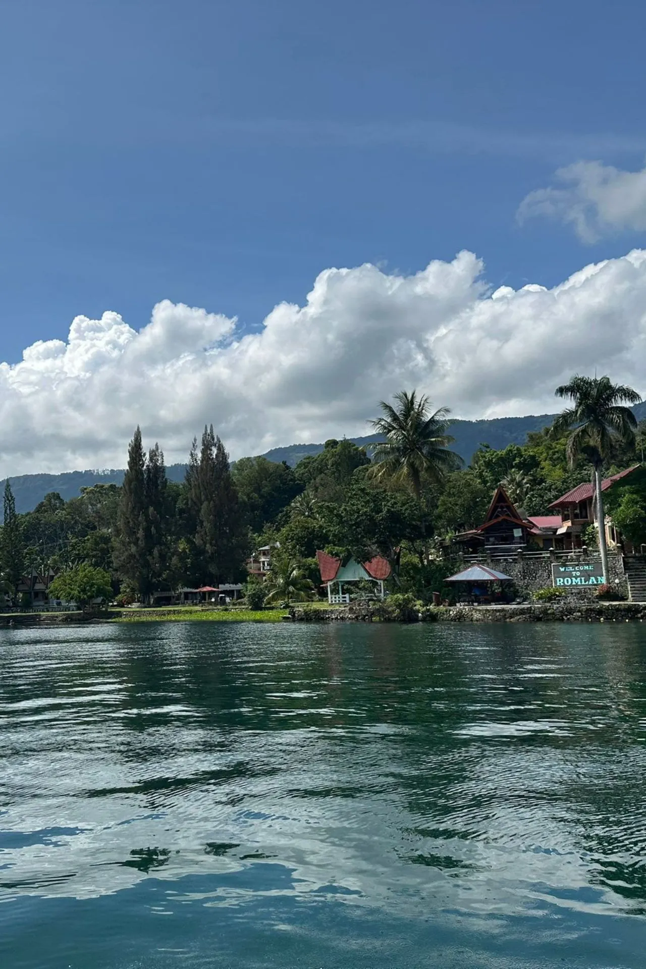Een serene aanblik van het Tobameer op Sumatra, omringd door weelderige groene heuvels en traditionele huizen aan de oever.
