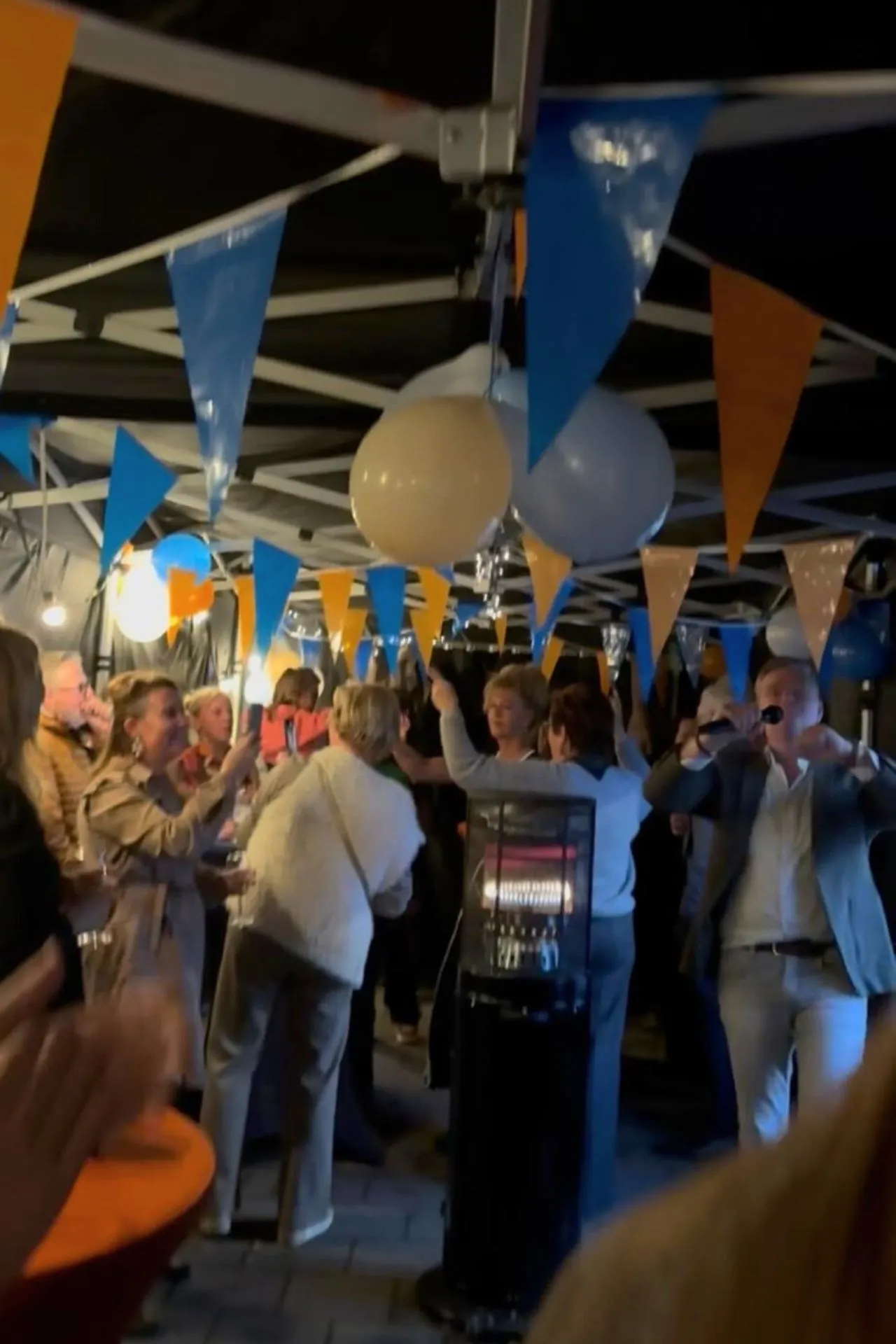 Gezellige sfeer tijdens het besloten openingsfeest van Travelcenter de Wit Asten, met kleurrijke vlaggetjes, ballonnen en gasten die proosten onder een feesttent.