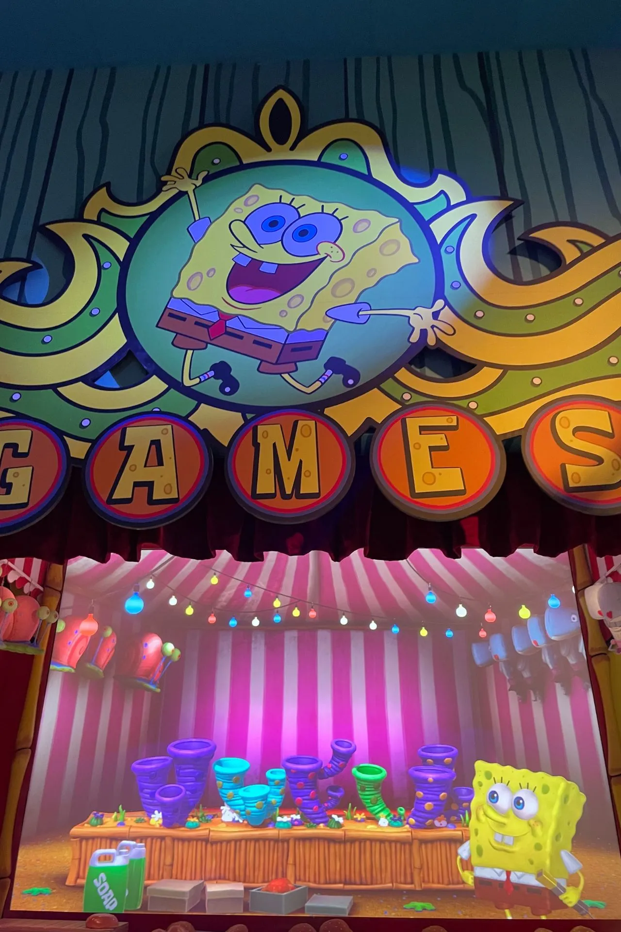 Games-ruimte met een groot SpongeBob-bord en kleurrijke animaties op een scherm, omringd door speelse verlichting.