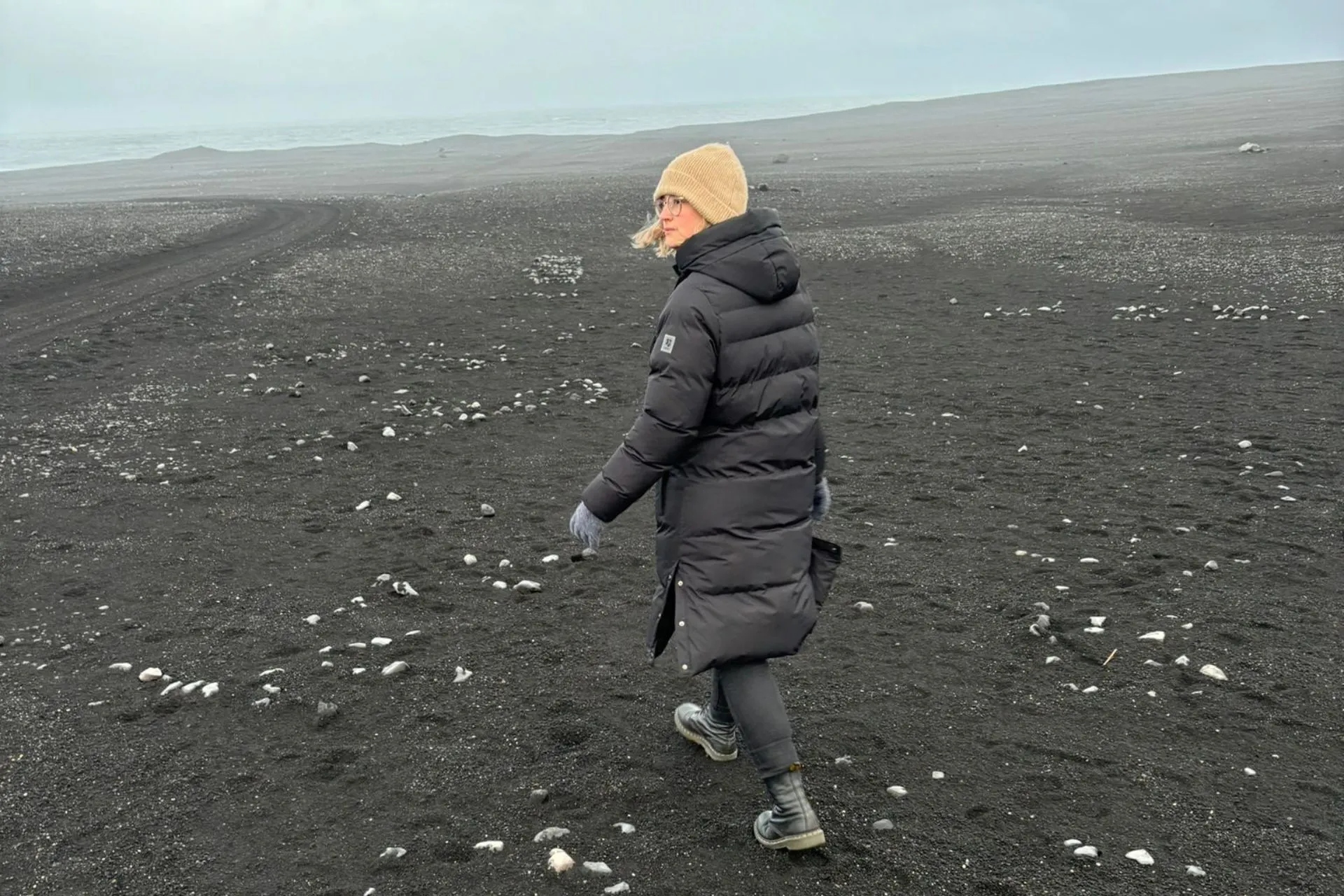 Reisadviseur Vera wandelt over een uitgestrekt zwart zandstrand met verspreide witte steentjes in Reykjanes, IJsland.