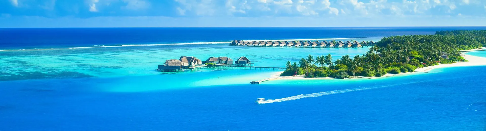 Luchtfoto van een tropisch eiland op de Malediven met luxe waterbungalows, turquoise lagunes en een helderblauwe zee onder een deels bewolkte hemel