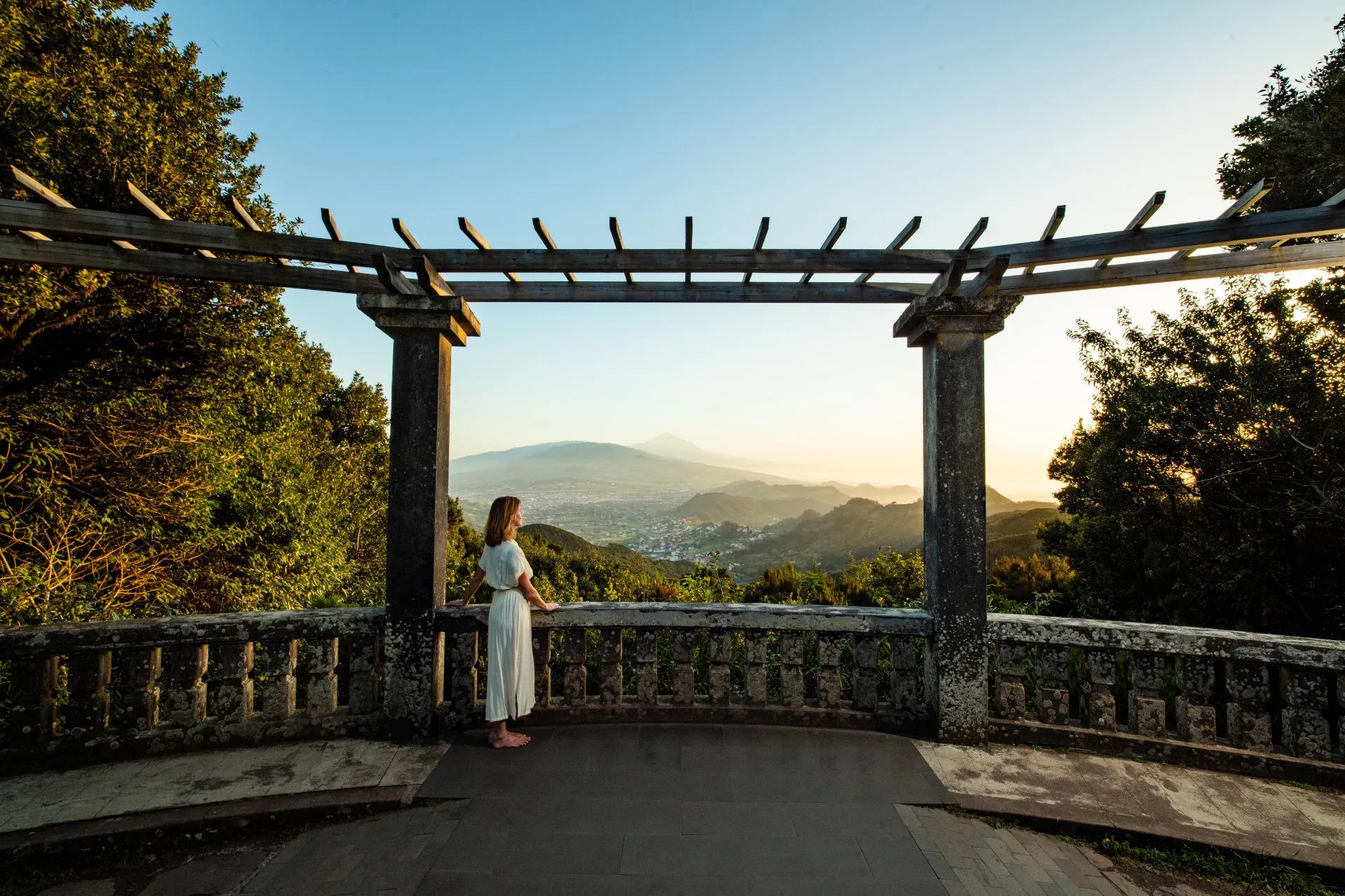 Uitzichtpunt met pergola en panorama over bergen en vallei bij zonsondergang
