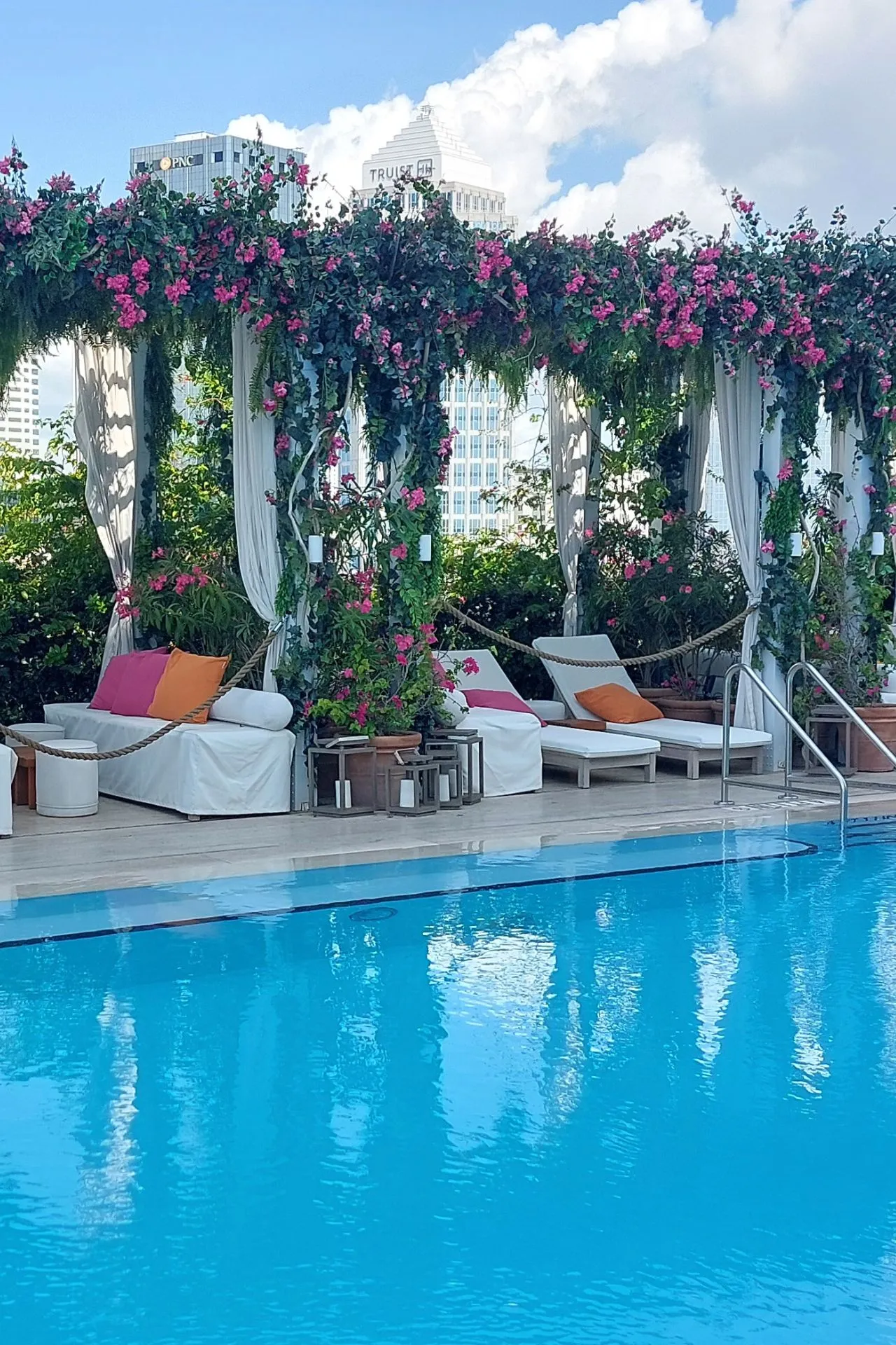Zwembad van JW Marriott Tampa Water Street, omringd door luxe cabana's met kleurrijke kussens en bloeiende roze bloemen onder een blauwe hemel.