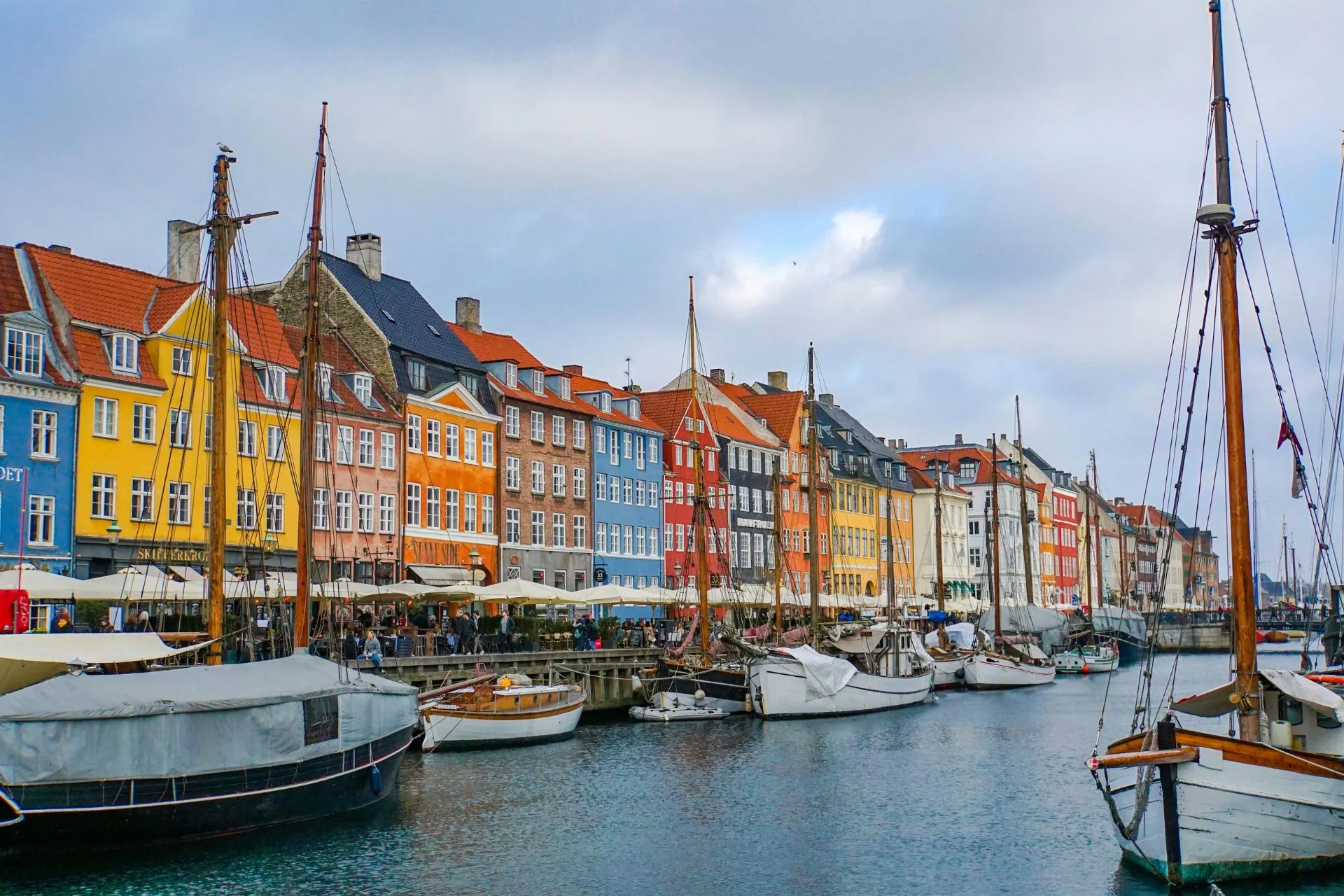 Kleurrijke huizenrij langs de Nyhavn haven in Kopenhagen met aangemeerde boten en een levendige sfeer.