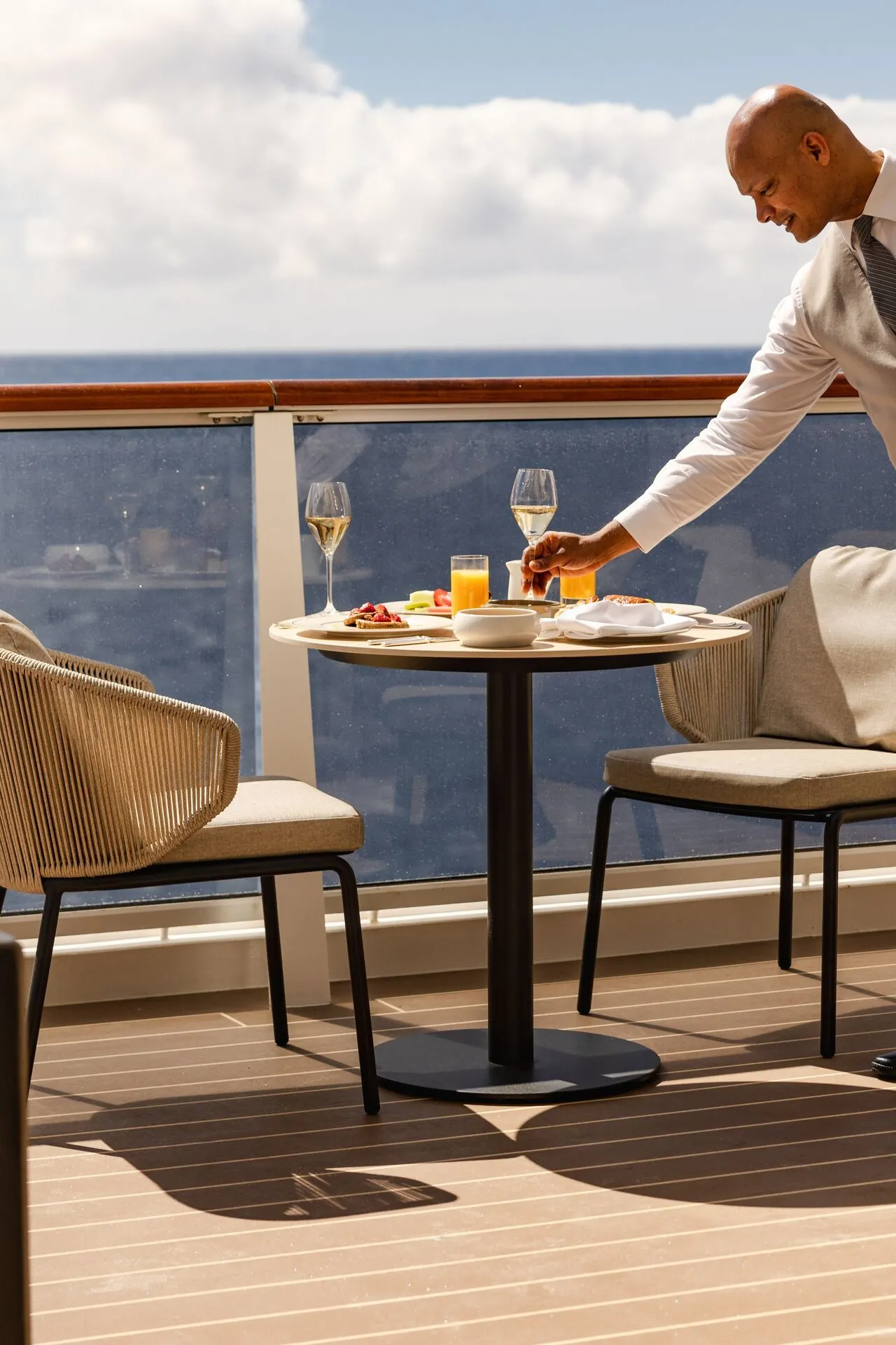 Luxe cruise-ervaring op het balkon van een Explora Cruise schip, met een prachtig uitzicht op zee en een stijlvolle opstelling van een ontbijttafel met verse jus, champagneglazen en elegante stoelen. Een attente crew serveert een verfijnde maaltijd, wat de ultieme combinatie van comfort, exclusieve service en ontspanning benadrukt. Ontdek waarom Explora Journeys bekendstaat als dé keuze voor een luxe cruisevakantie met culinaire hoogstandjes en adembenemende bestemmingen.