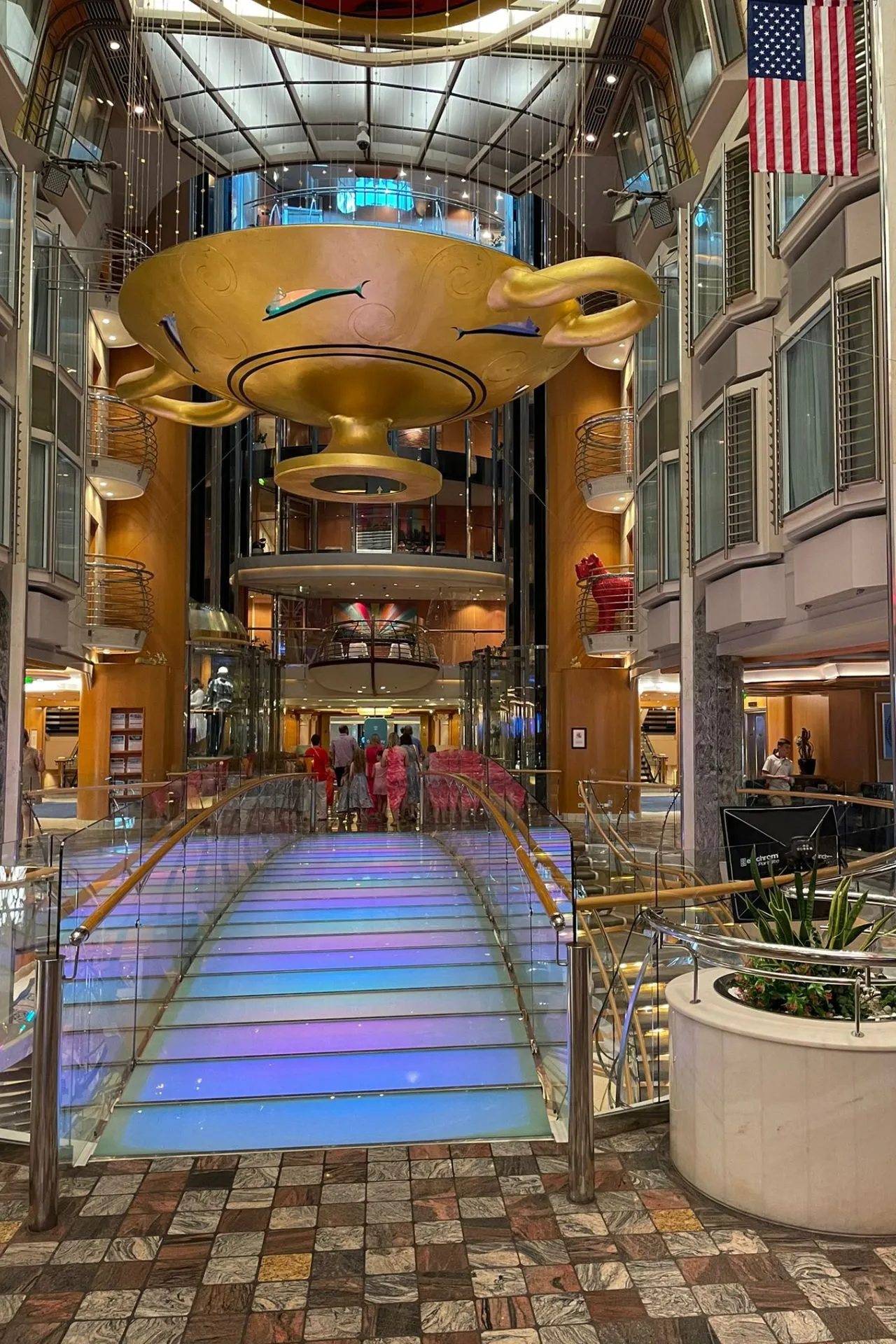 gouden kunstinstallatie bovenin en passagiers die door de winkelstraat wandelen.