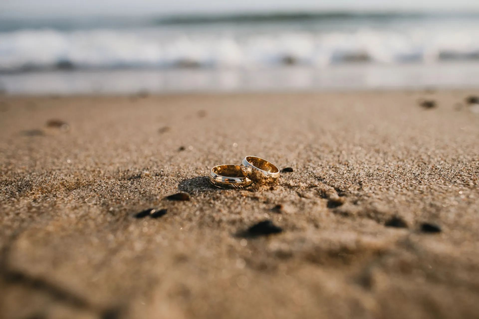 Twee verlovingsringen liggen sierlijk in het zand van het strand, de zonsondergang werpt een warme gloed over het moment, symbolisch voor de belofte van een leven samen.
