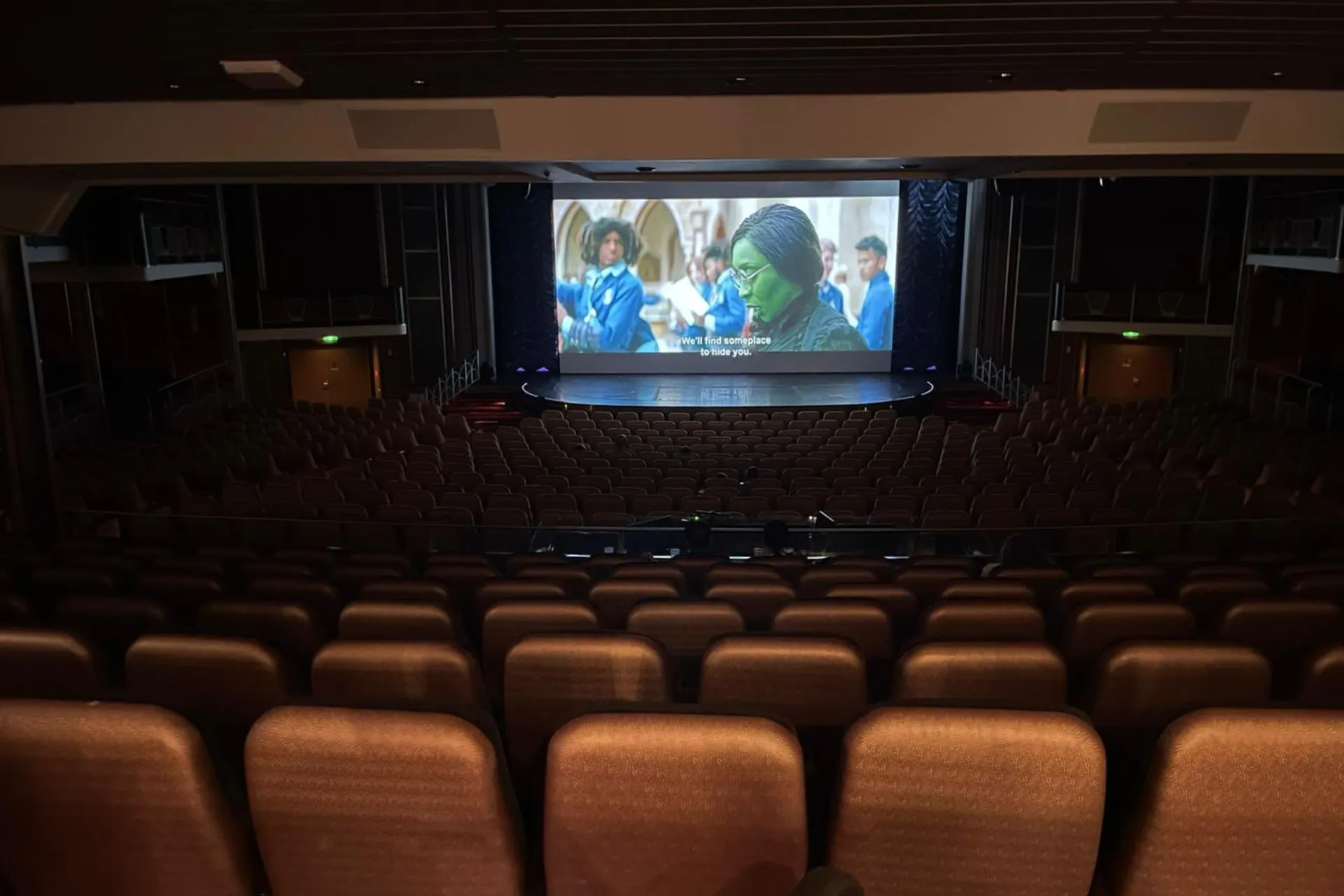 Groot theater aan boord van de Independence of the Seas, met rijen comfortabele stoelen en een filmscherm waarop een film met ondertiteling wordt vertoond.