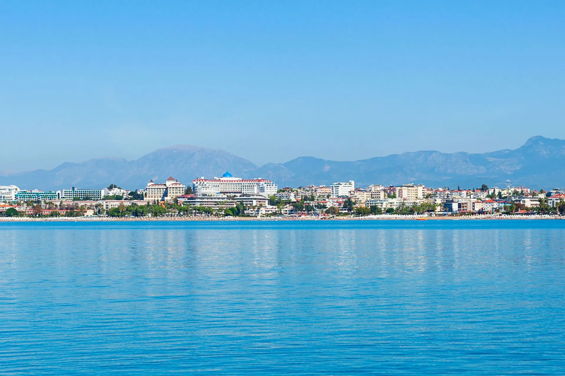 Panoramisch uitzicht op de kust van Side met moderne hotels, uitgestrekte stranden en de bergen van het Taurusgebergte op de achtergrond. Vanaf het water is goed te zien hoe natuur, zee en vakantievoorzieningen samenkomen. Side is een geliefde badplaats aan de Turkse Rivièra en een ideale uitvalsbasis voor excursies.
