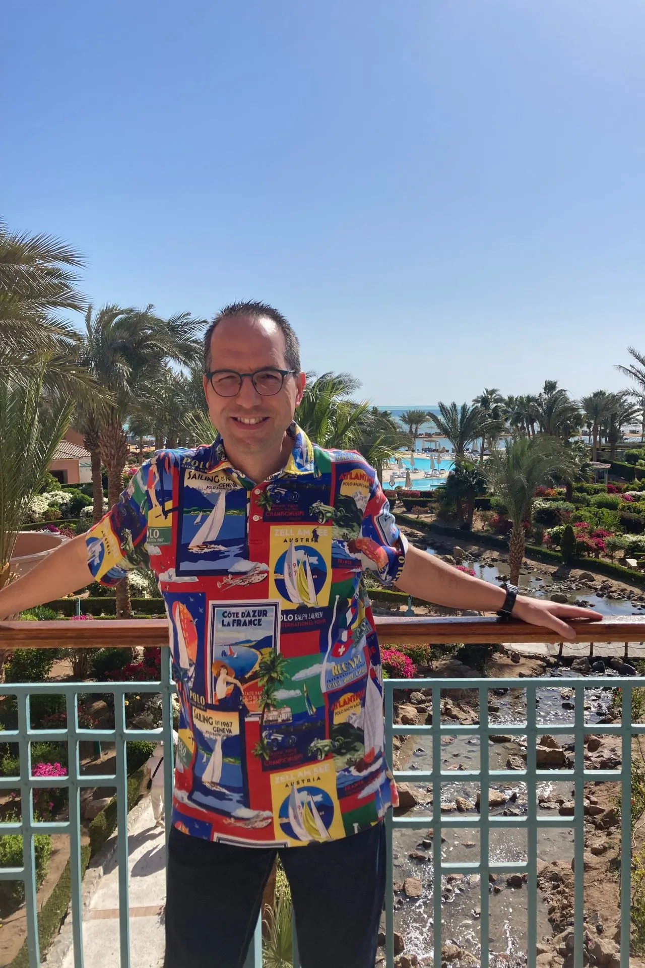 
Reisspecialist Dino staand op een balkon in El Gouna, Egypte, met uitzicht op tropische tuinen, palmbomen en zwembaden van een luxe resort. Op de achtergrond de Rode Zee en strakblauwe lucht, wat de ontspannen vakantiesfeer en het zonnige klimaat van El Gouna laat zien.