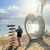 Zonnige vakantiesfeer op het strand van Jamaica met een blonde dame, een wit rieten hart en een vrolijk gekleurde wegwijzer.