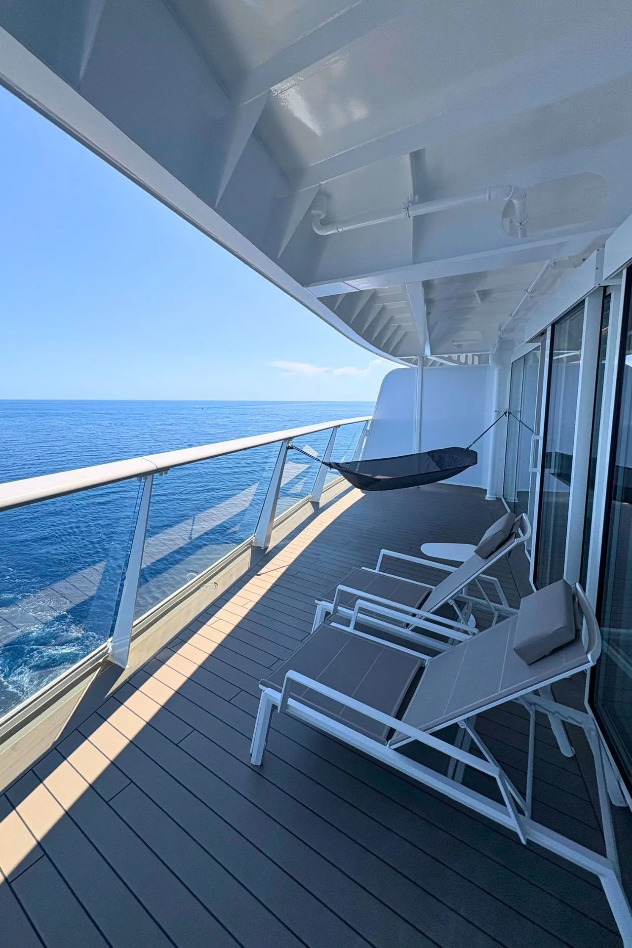 Ruim balkon van een suite aan boord van de Mein Schiff Flow met ligbedden, een hangstoel en panoramisch uitzicht over zee. Deze luxe buitenruimte biedt gasten volop privacy en comfort tijdens de cruise. Dankzij de royale afmetingen is dit de ideale plek om te ontspannen, te zonnen of te genieten van de voorbijglijdende horizon.