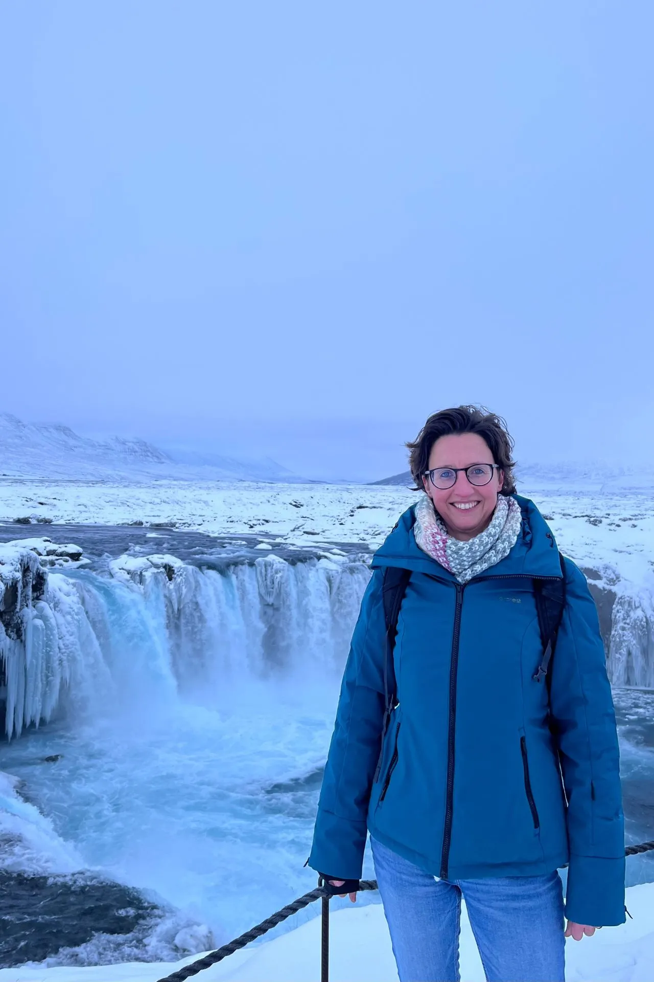 Reisspecialist Susan Wolfs bij de besneeuwde Godafoss‑waterval in Noord‑IJsland tijdens de winter.