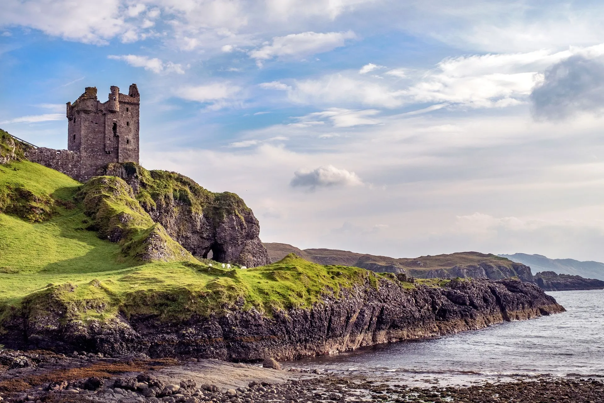 Een ruïne van een oud kasteel op een groene klif aan de Schotse kust, met de oceaan en heuvelachtig landschap op de achtergrond.