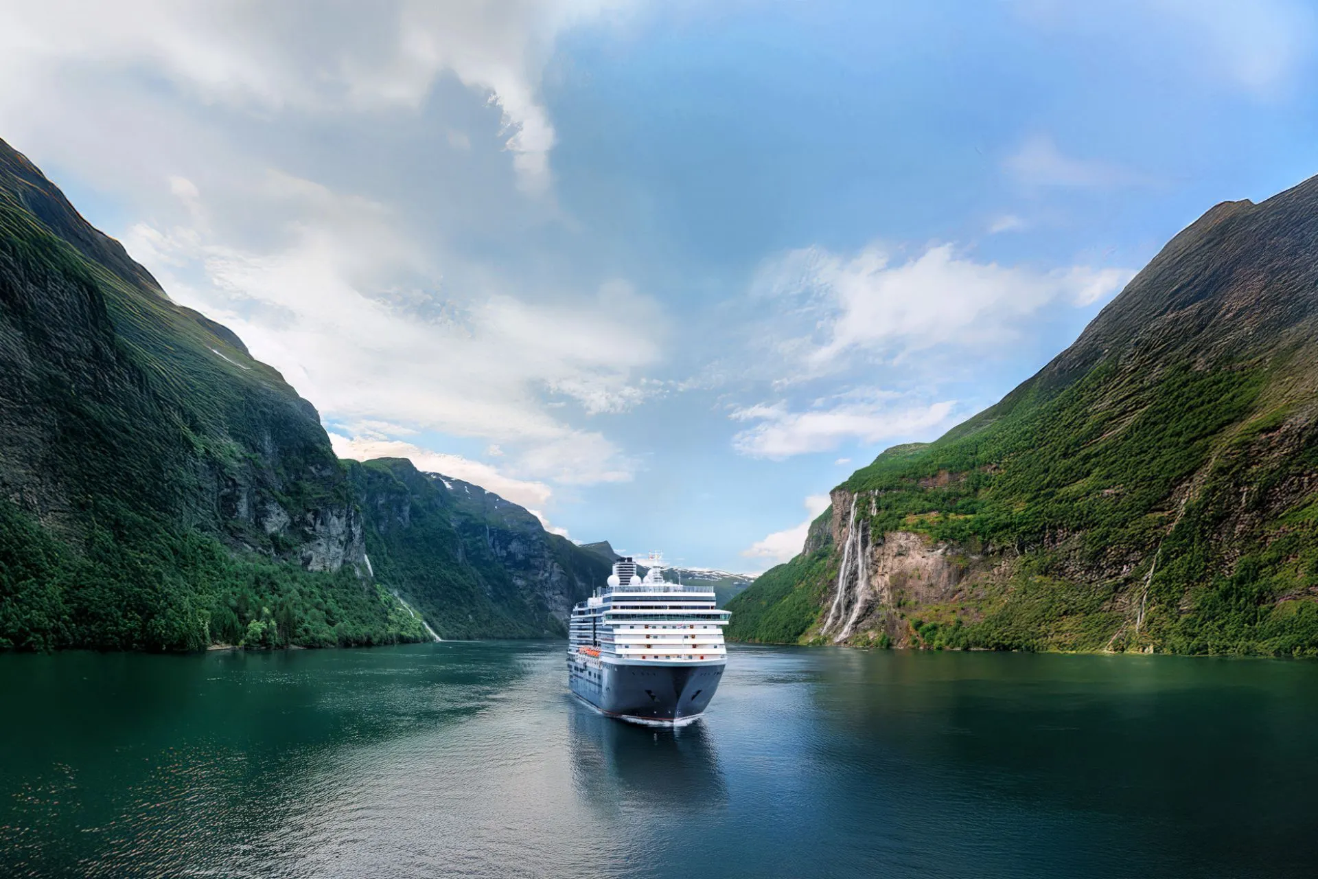 Holland America Line cruiseschip vaart door een schilderachtige Noorse fjord met hoge groene bergwanden en watervallen op de achtergrond.