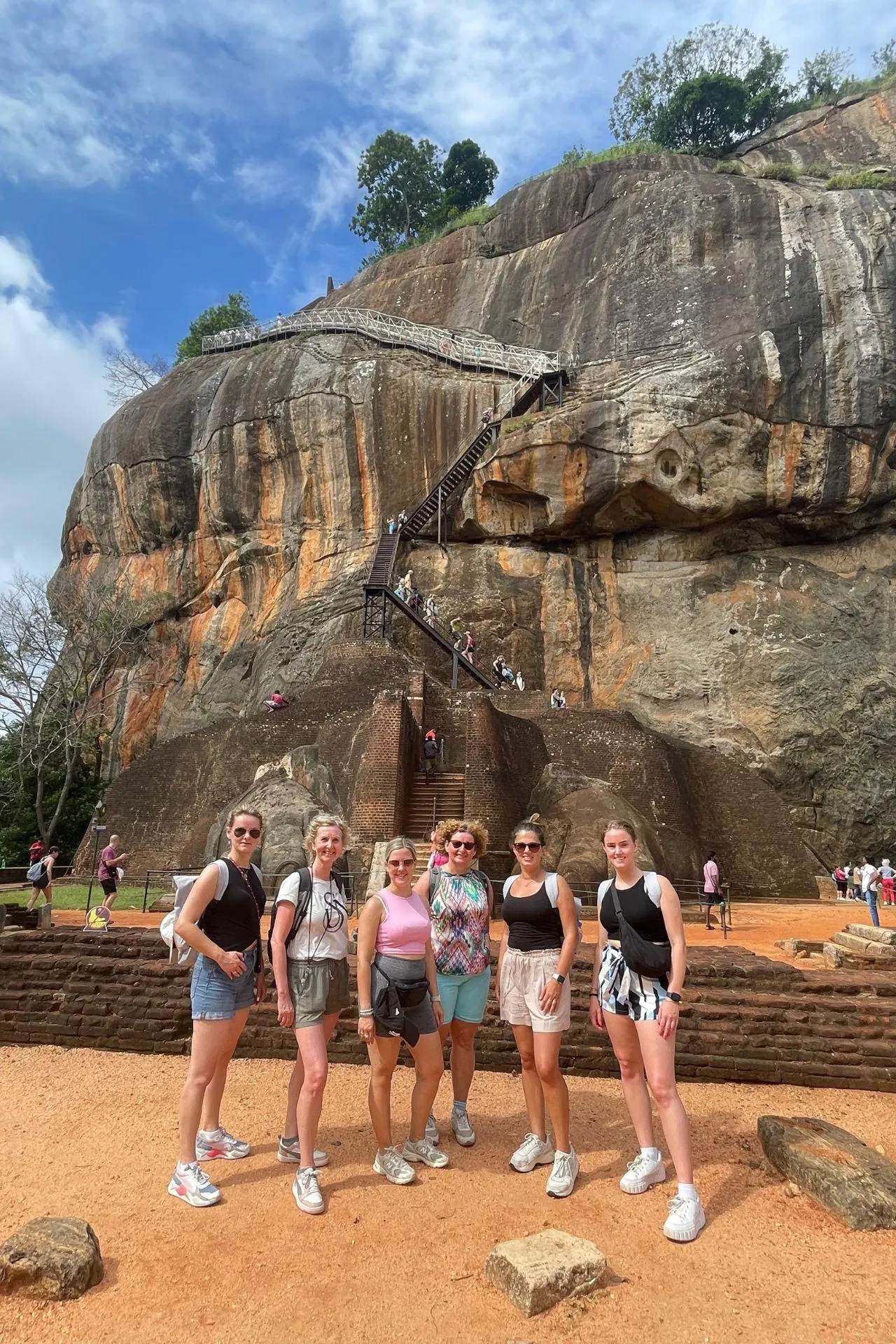 Groep vrouwen poseert voor de Leeuwenrots in Sigiriya, Sri Lanka, met de trap naar de top op de achtergrond.