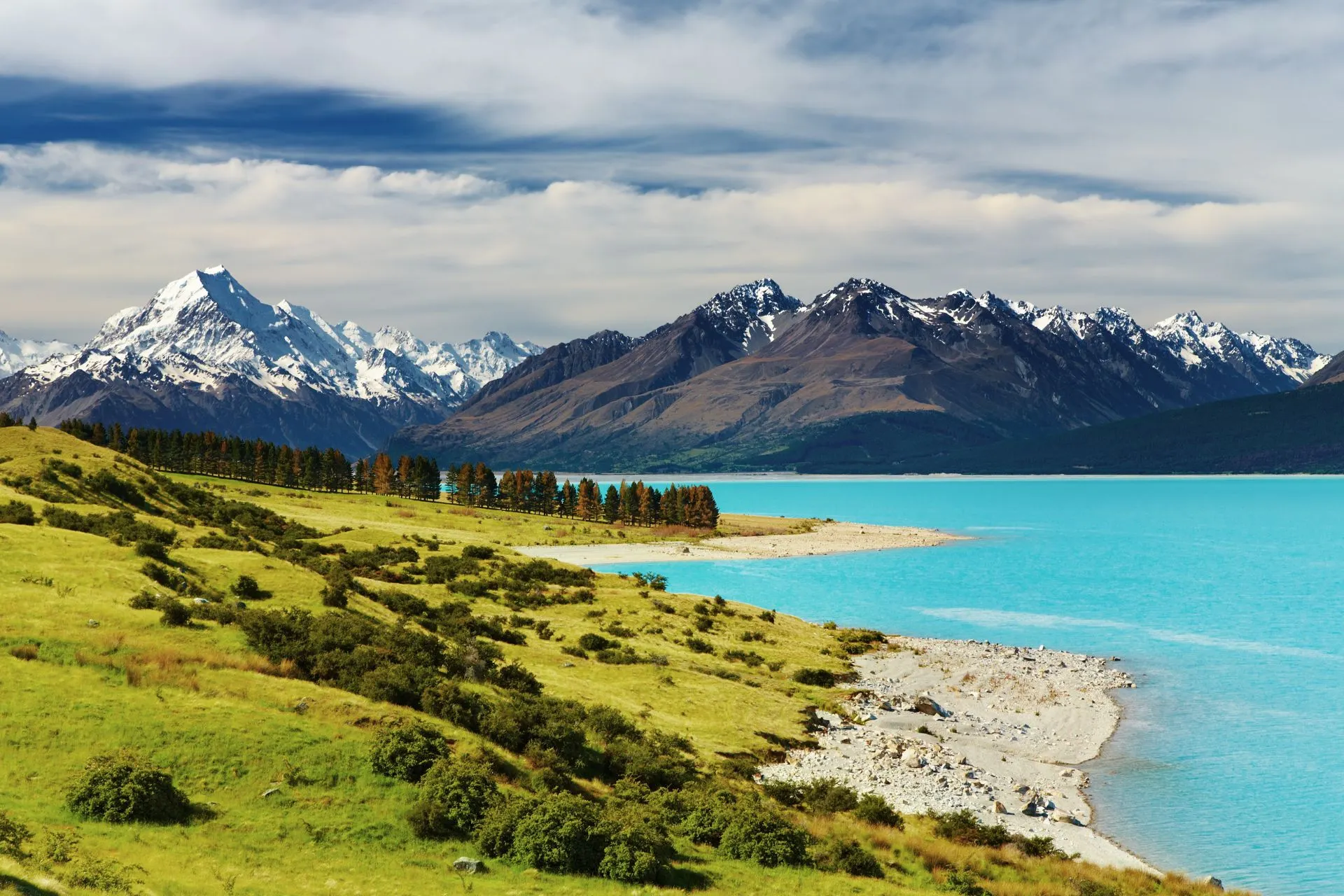 Turquoise meer met groene heuvels en besneeuwde bergen op de achtergrond in het Zuidereiland van Nieuw‑Zeeland.