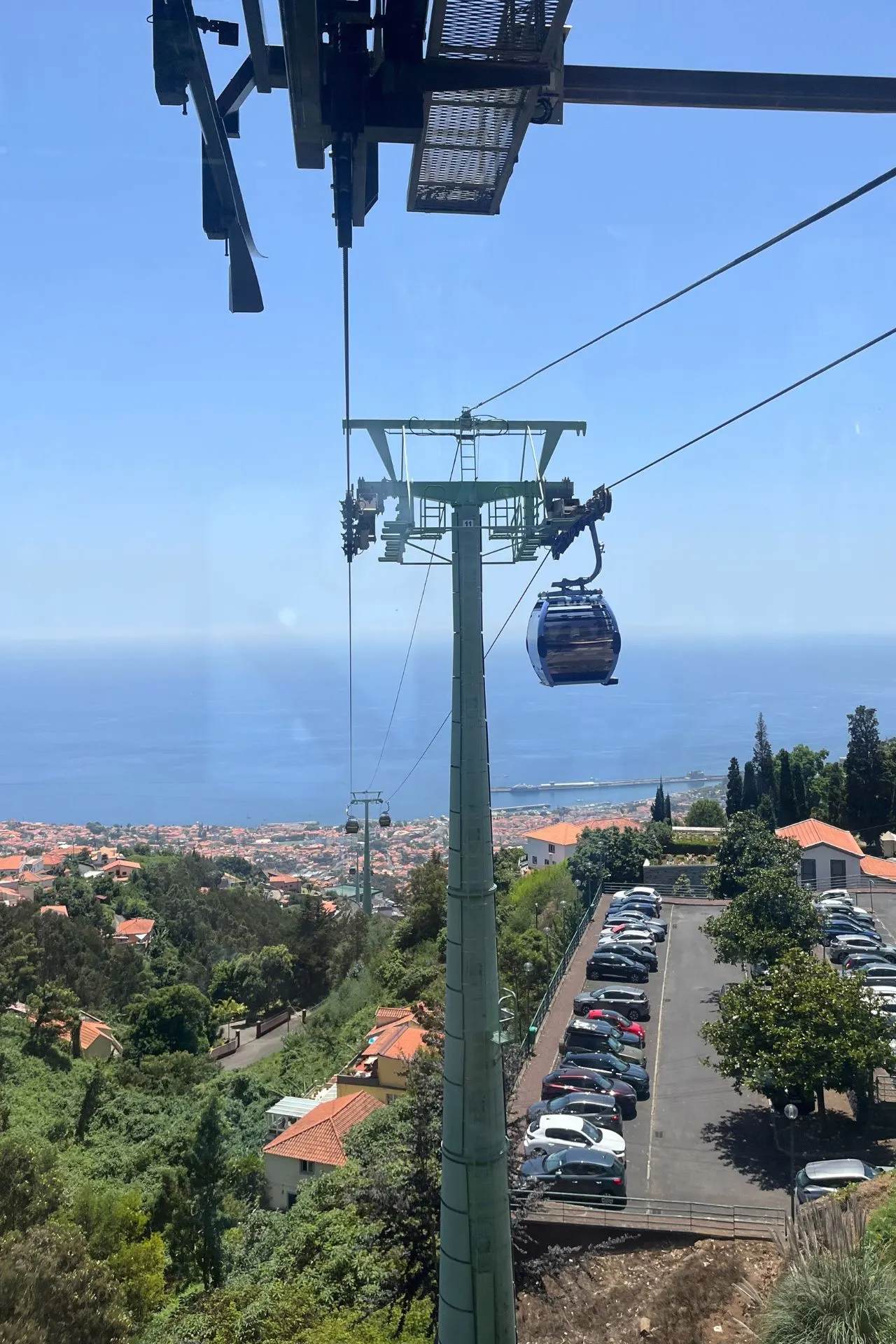 Kabelbaan in Funchal zweeft boven groene heuvels en huizen met de Atlantische Oceaan op de achtergrond.